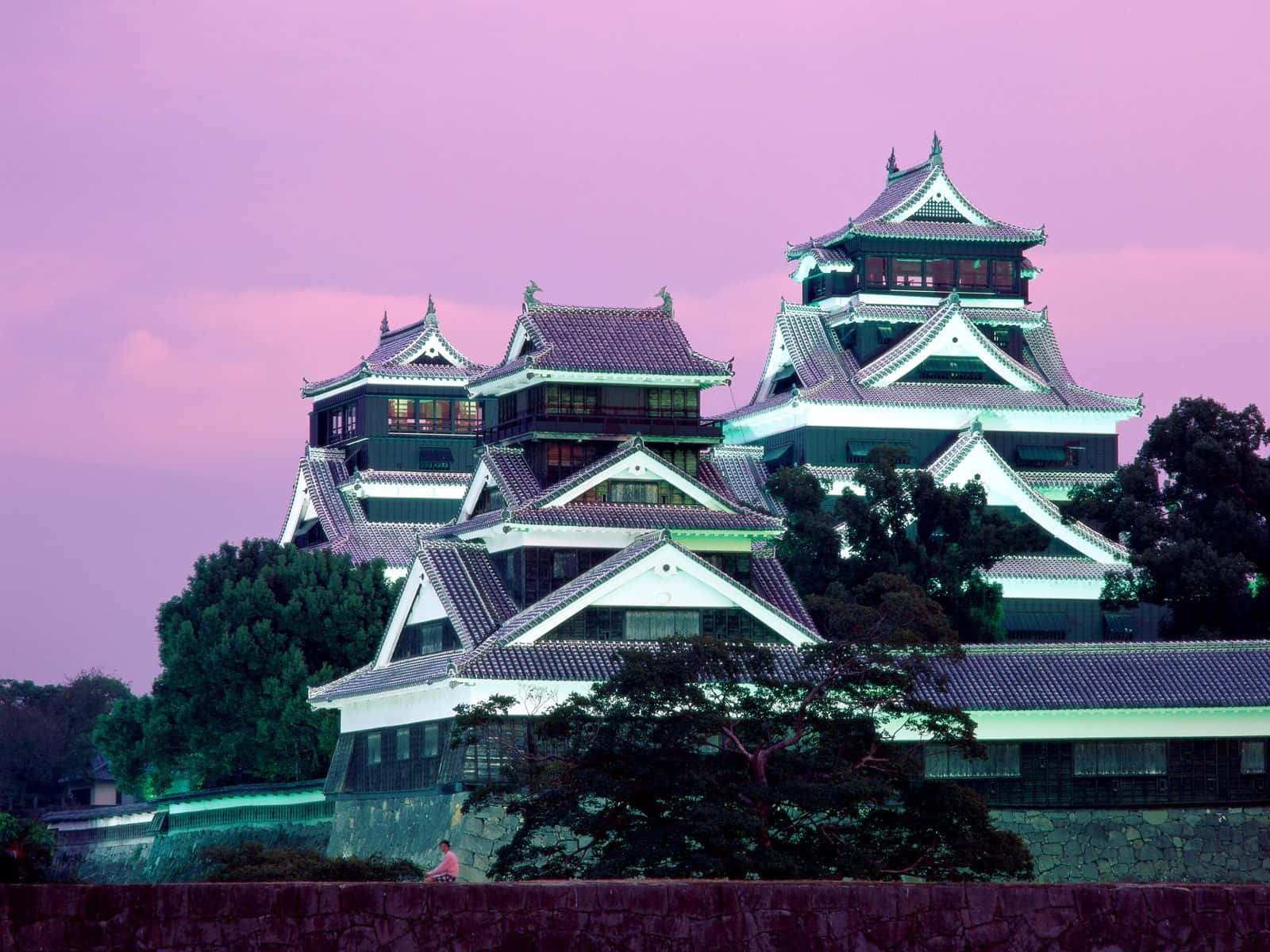 傳統日本城堡在暮色中，粉紅色天空和綠色樹木。