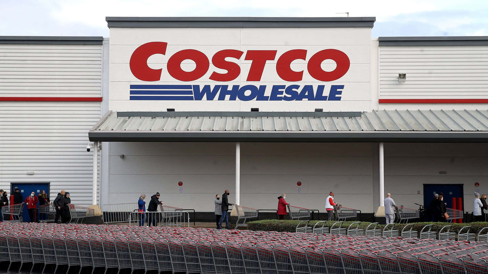多雲天氣下，人們在Costco商店外推著購物車。