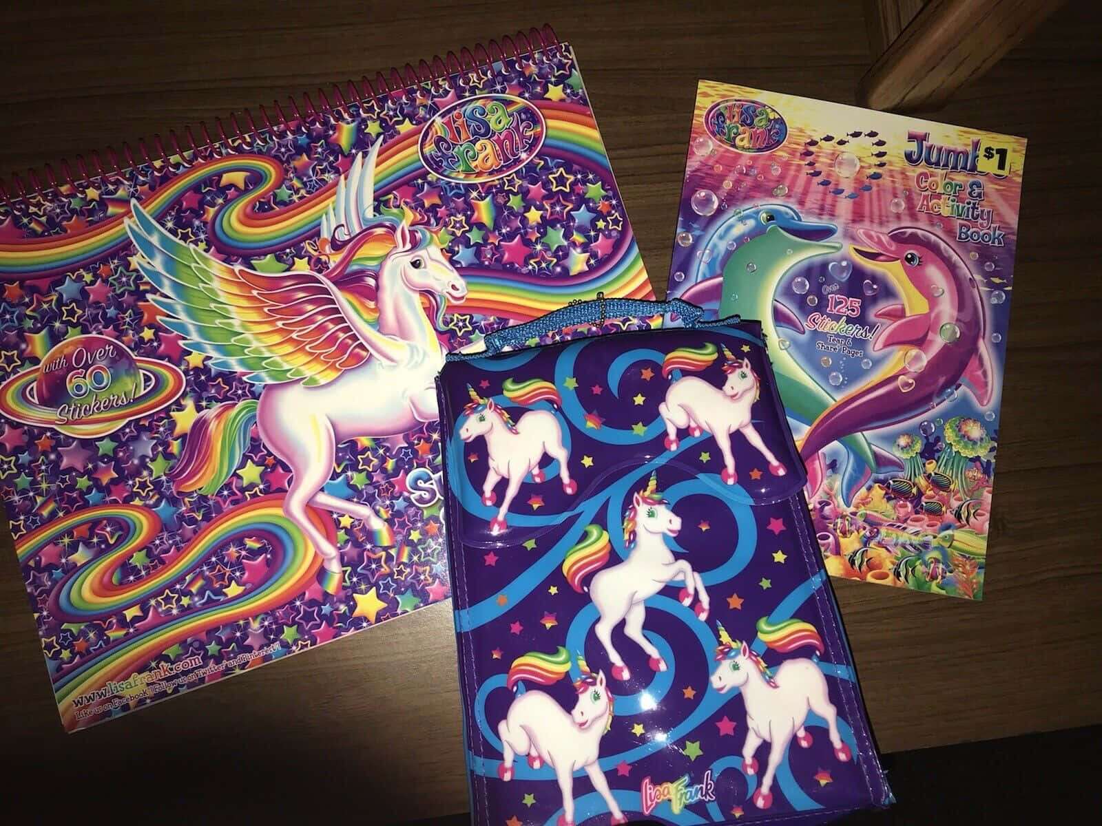 三本獨角獸活動書和一個帶有彩虹翅膀和星星的小袋放在木桌上。