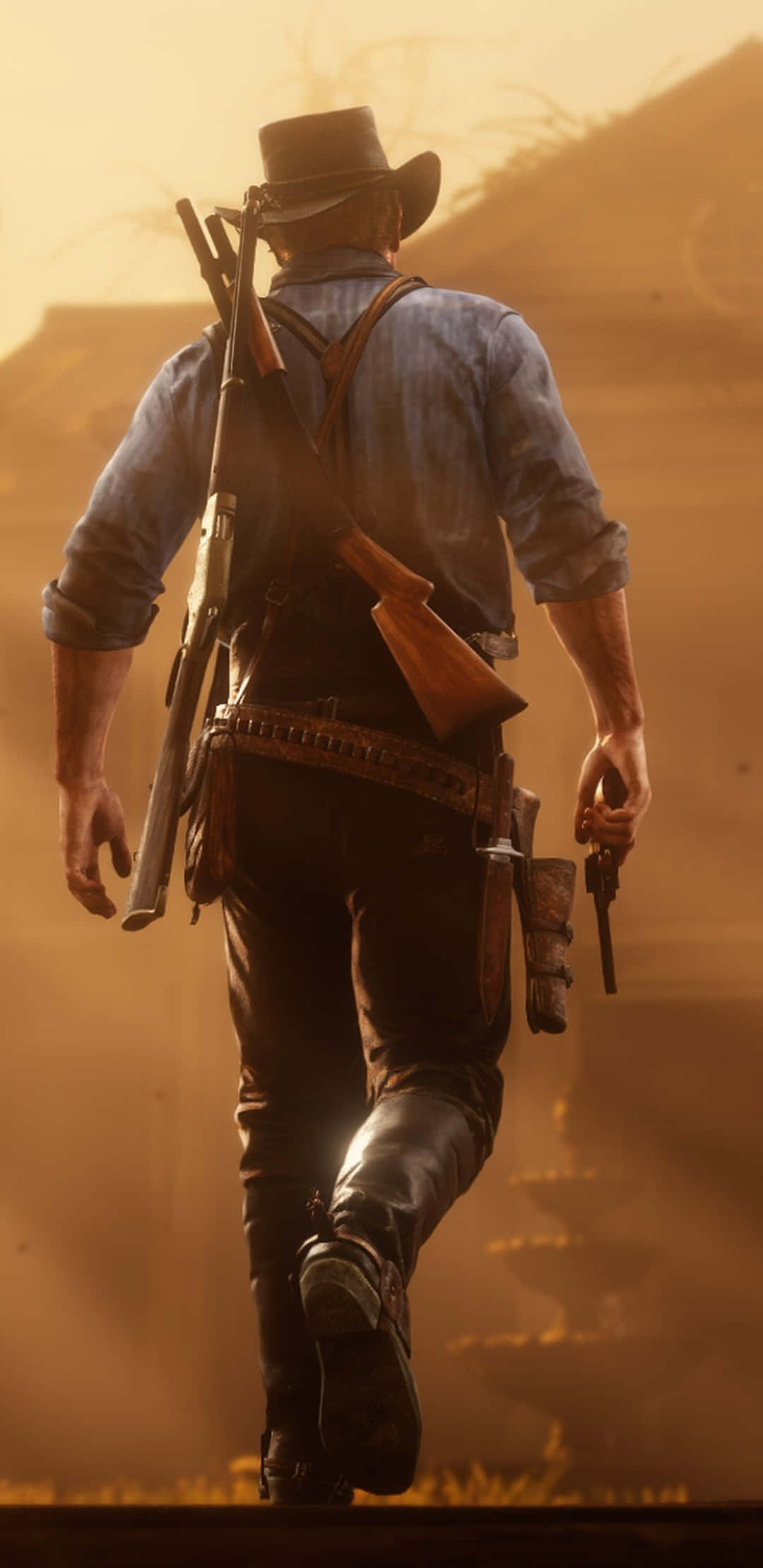 在安卓上體驗狂野西部：Red Dead Redemption 2 壁紙 — 一個孤獨的牛仔在日落時分帶著步槍和手槍走在塵土飛揚的西部風景中。