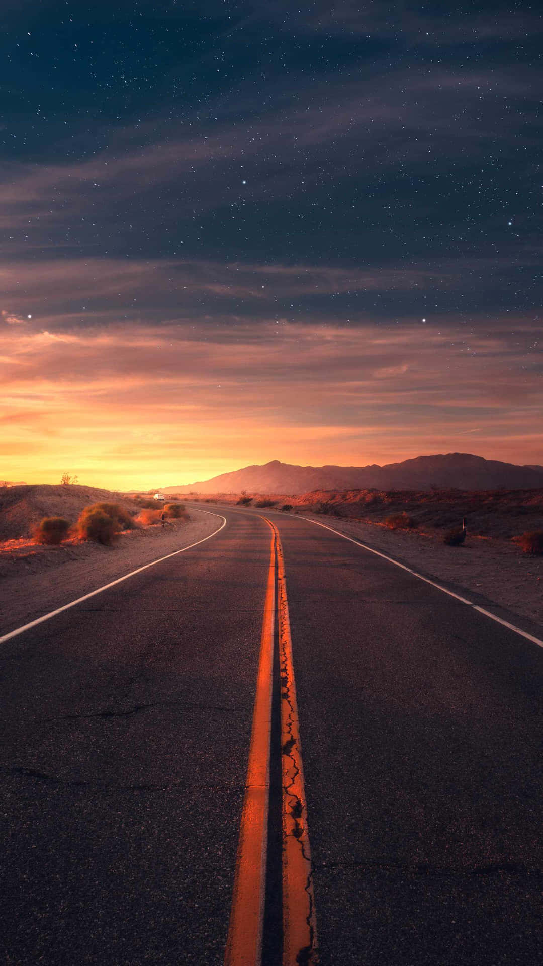 星空暮色下的沙漠公路，遠方有山脈