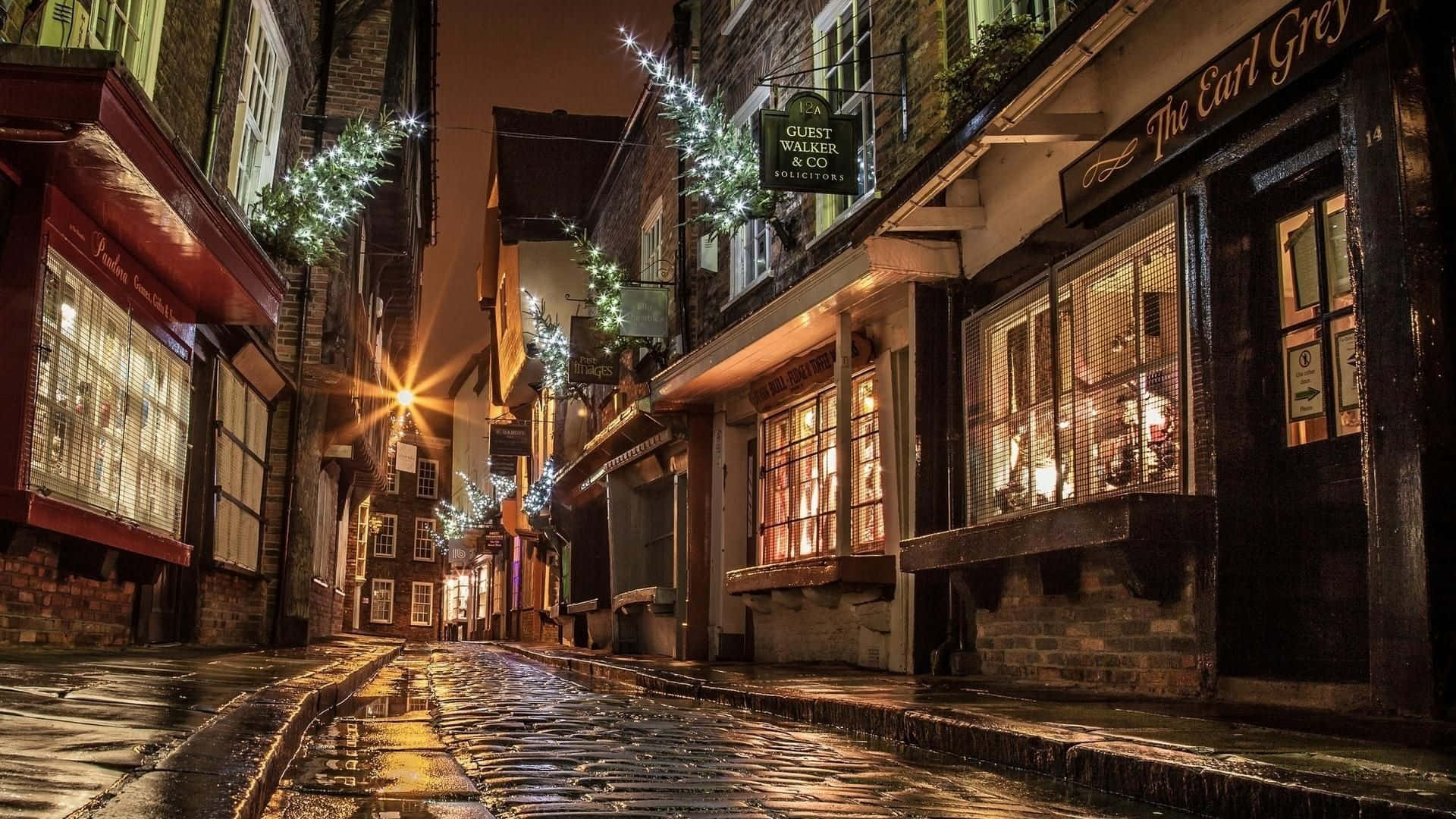 夜晚狹窄的鵝卵石街道，節日燈飾和閃爍的商店櫥窗。