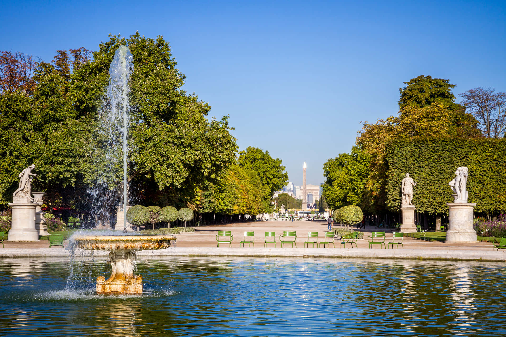 陽光明媚的公園中的大型噴泉，背景有雕像和城市天際線。