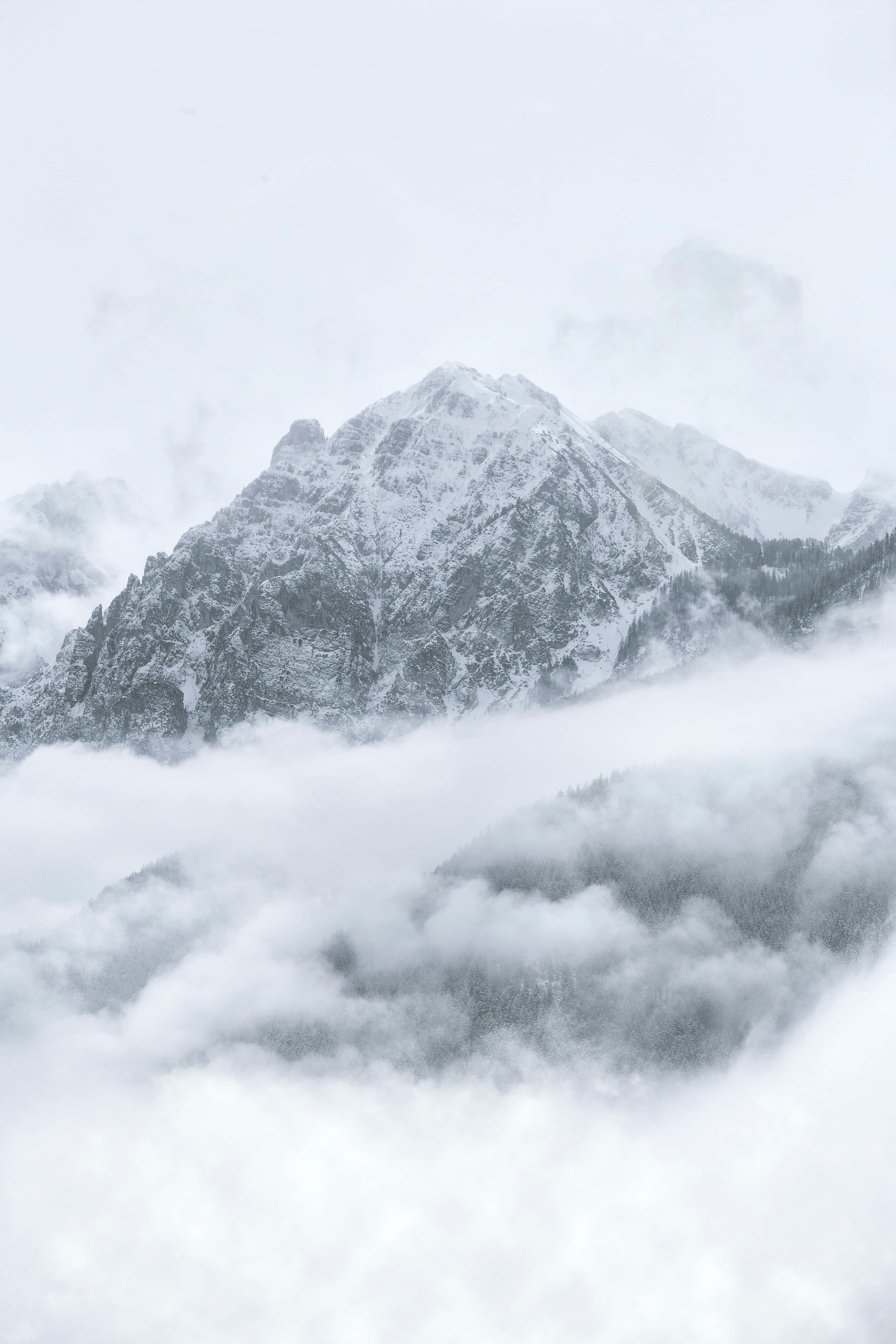 寒冷 桌布 壁紙 — 在寧靜的冬季景觀中，白雪覆蓋的山峰穿過厚厚的雲層。