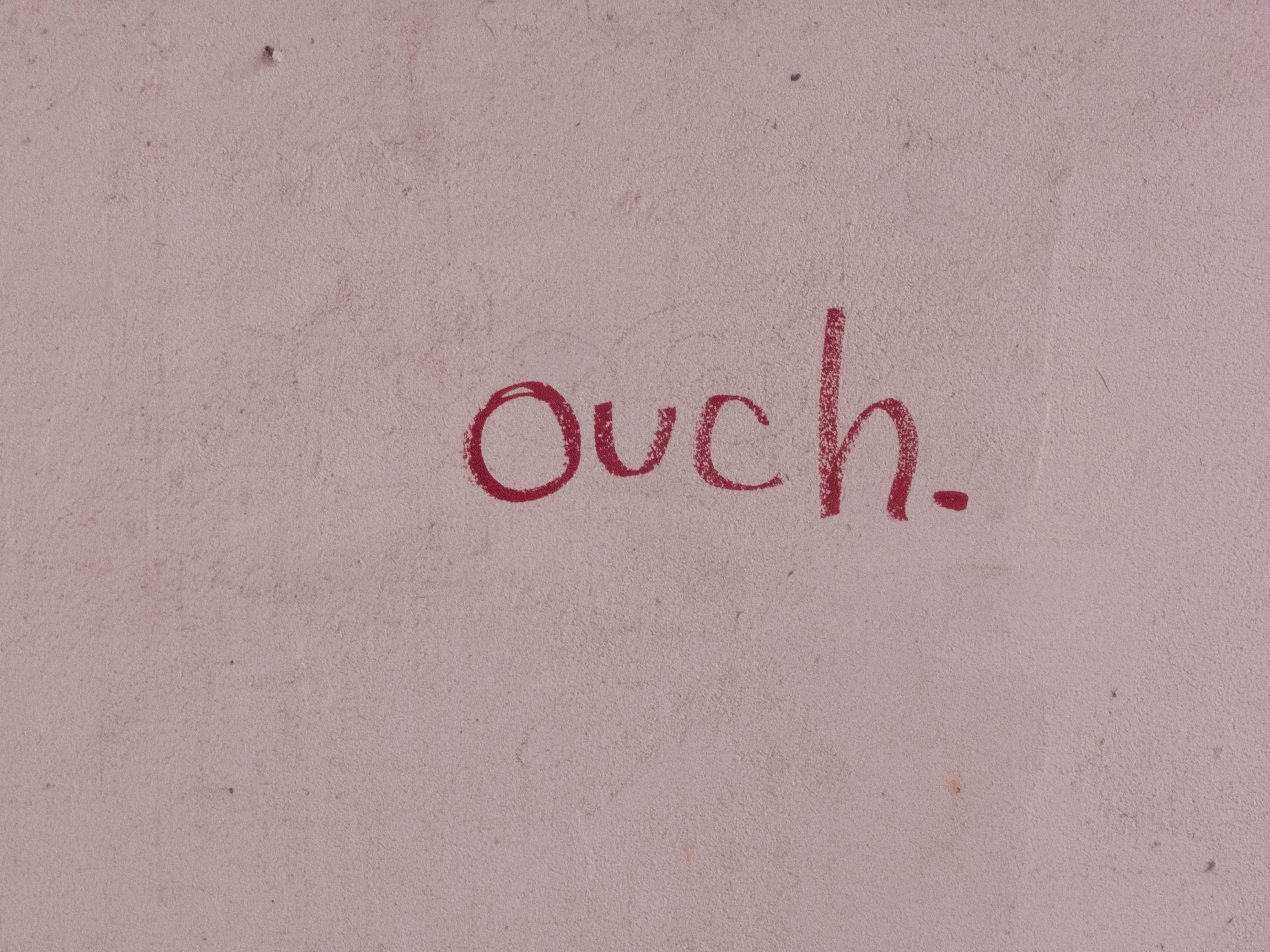 hurt 桌布 壁紙 — 在帶有紋理的淡粉紅色牆壁上用紅色粉筆寫的「ouch」一詞。