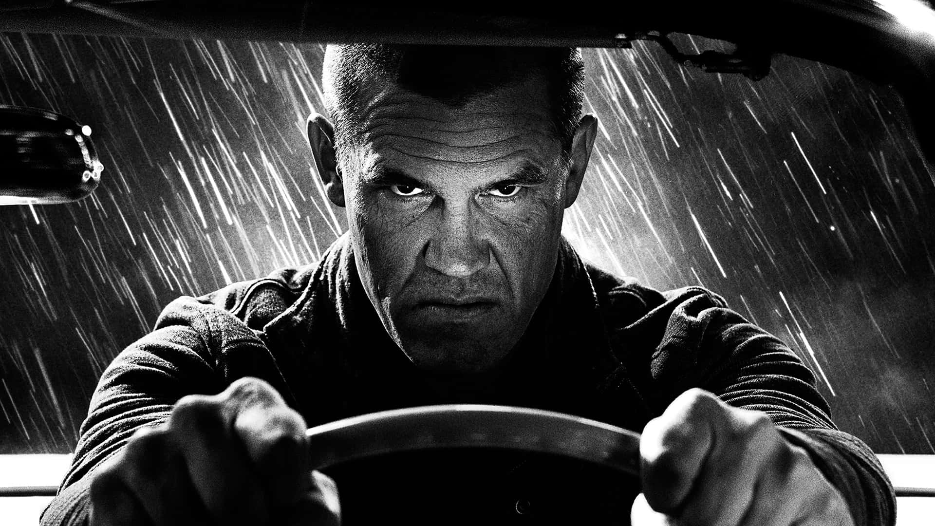 Josh Brolin 桌布 壁紙 — 在強烈對比的黑白照片中，一名男子在暴雨中緊握方向盤，神情專注。