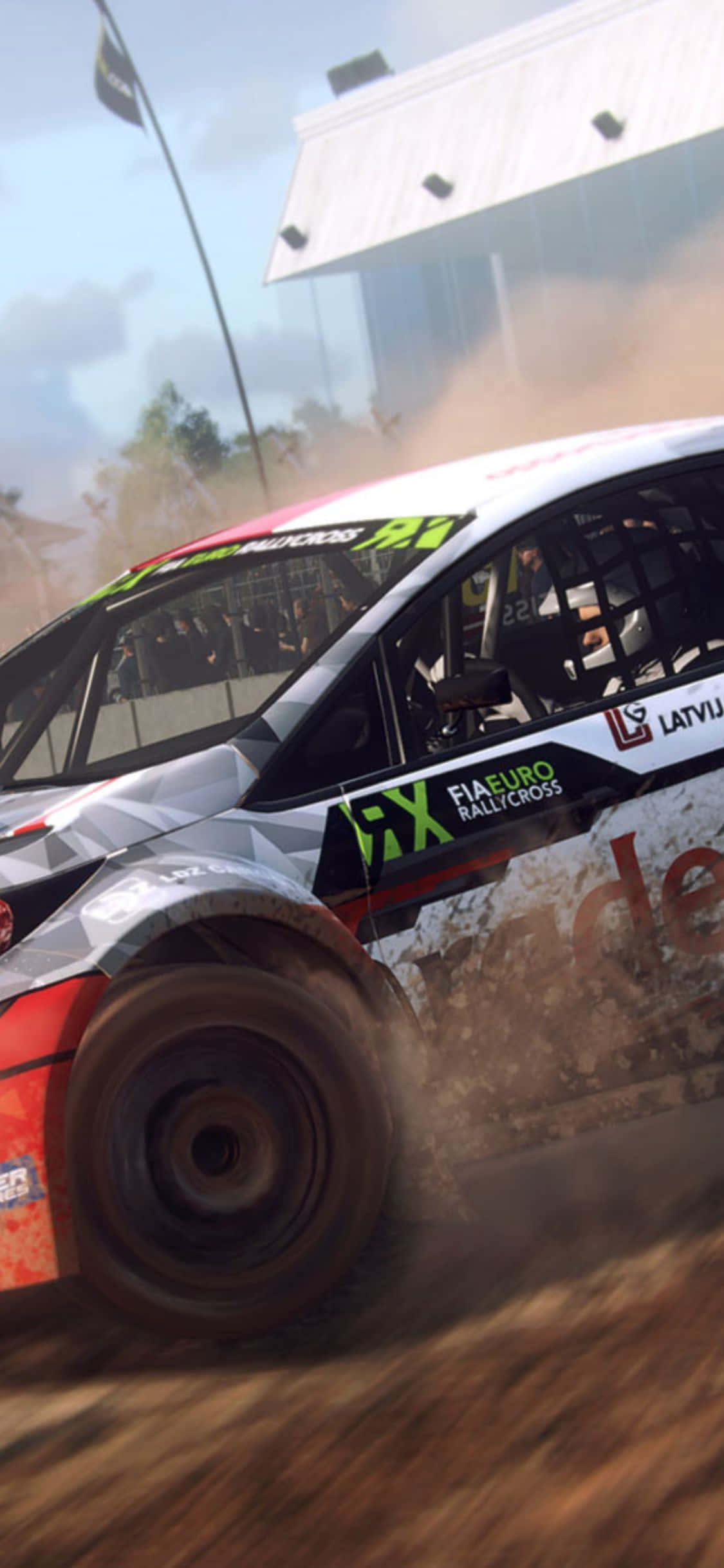 在您的 iPhone X 上體驗《Dirt Rally》的刺激 壁紙 — 一輛越野拉力賽車在塵土飛揚的賽道上疾馳，揚起塵土，背景有觀眾和一座現代建築。