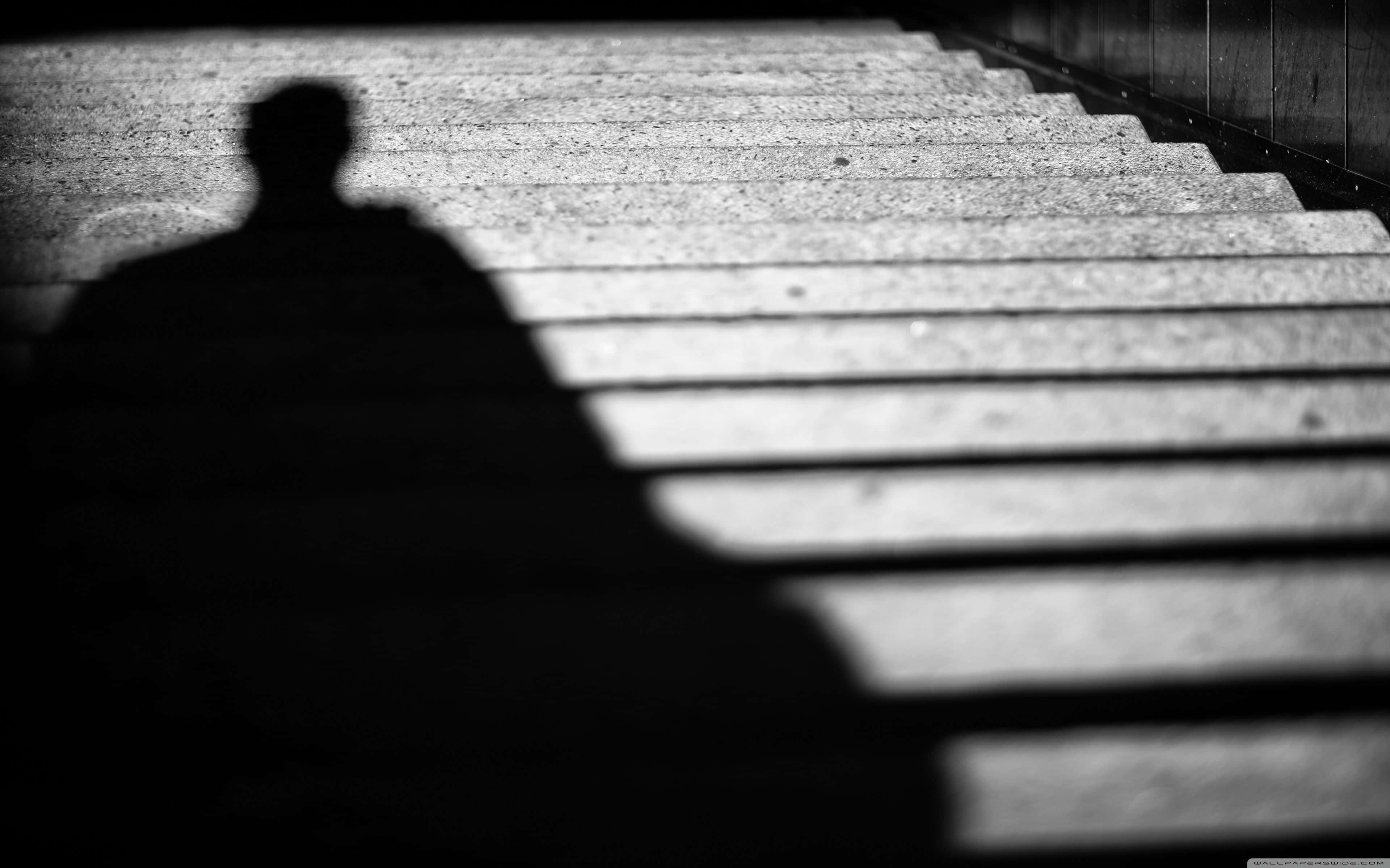 shadow 桌布 壁紙 — 在戲劇性燈光下，一個人的鮮明黑白影子走上混凝土樓梯。