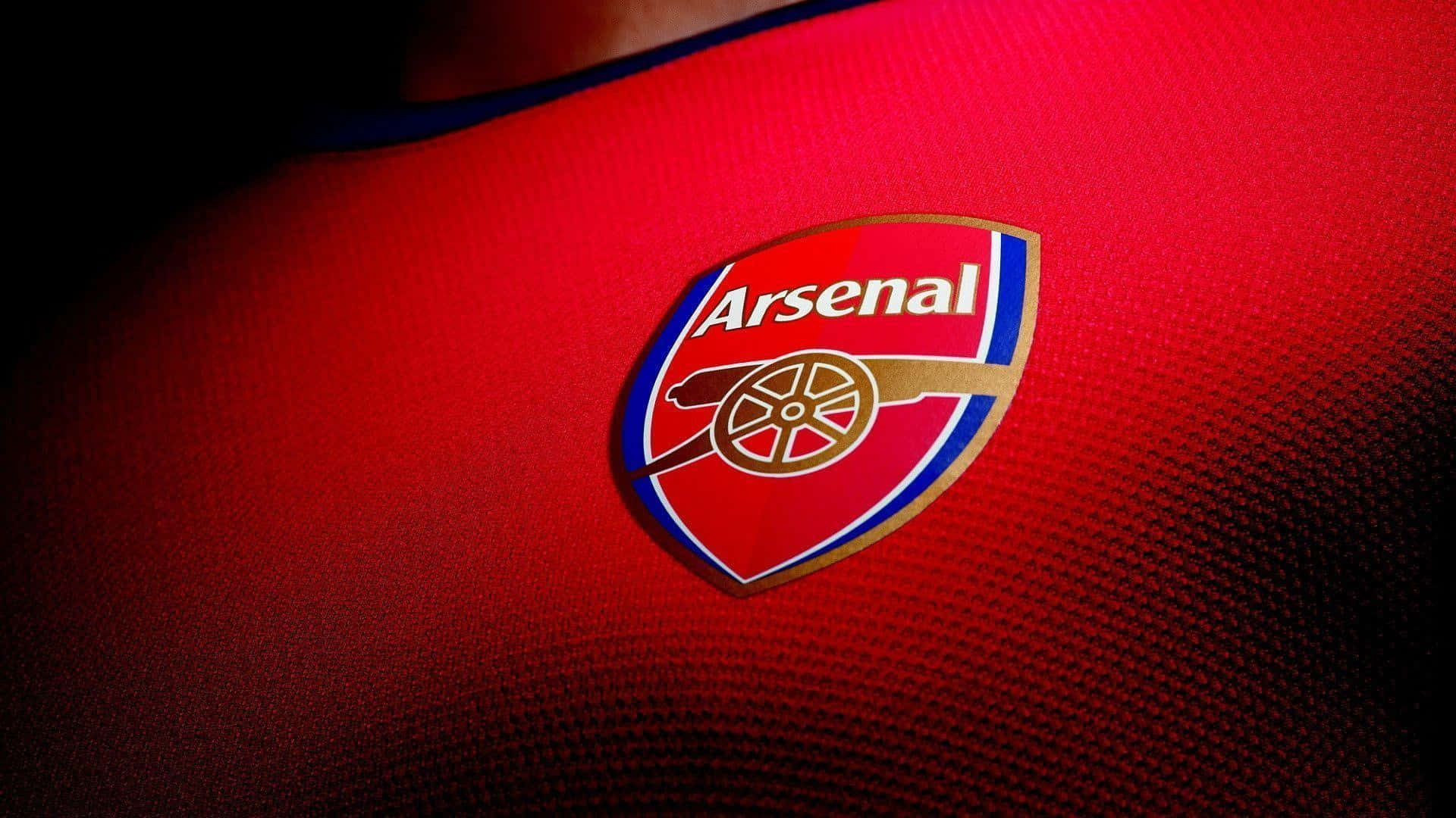 Arsenal 桌布 壁紙 — 在戲劇性燈光下，阿仙奴足球會徽章在帶有紋理的紅色足球球衣上的特寫。