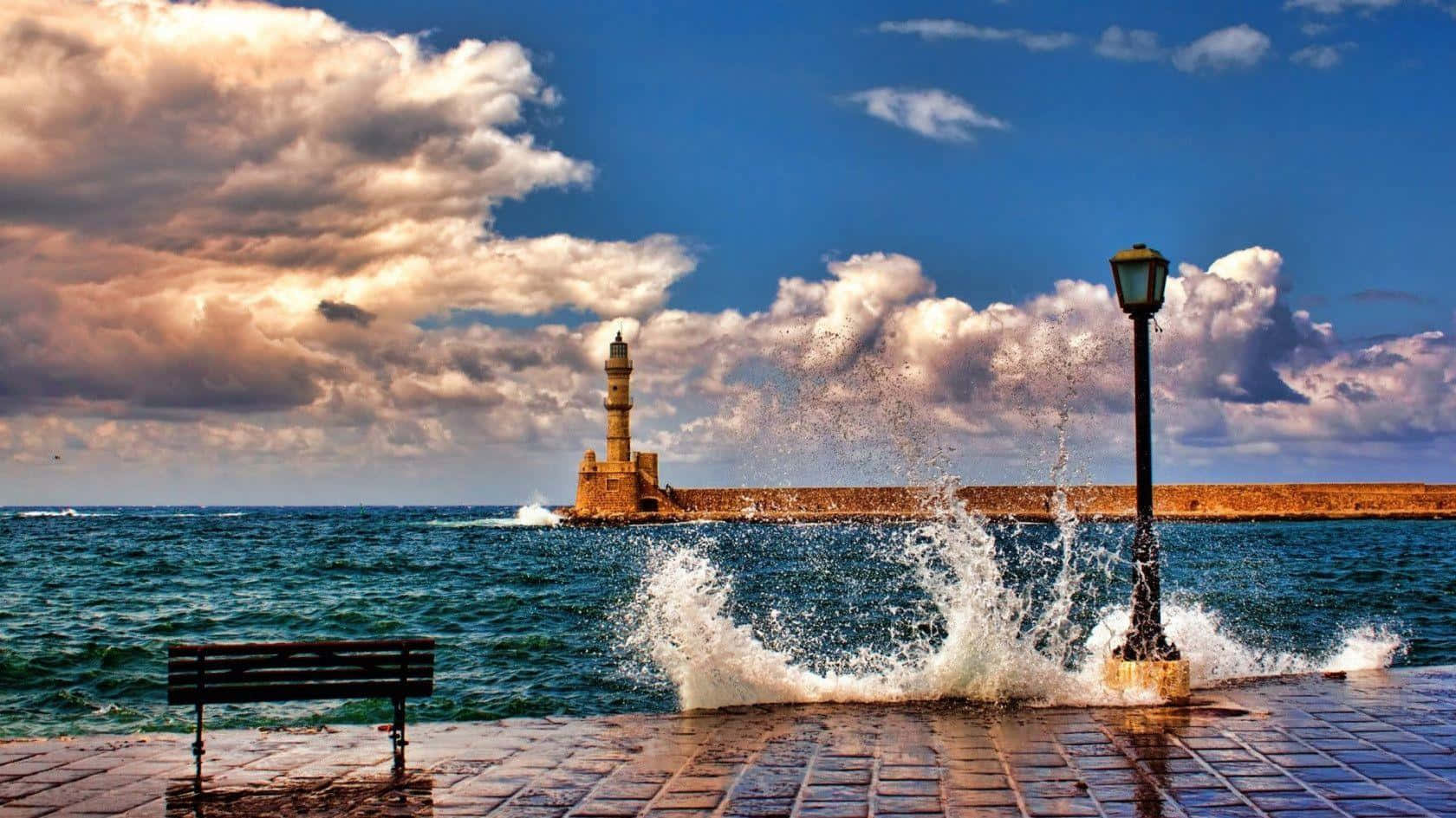 Beautiful Ocean 桌布 壁紙 — 在戲劇性的多雲天空下，強大的海浪沖擊著歷史燈塔附近的石碼頭。
