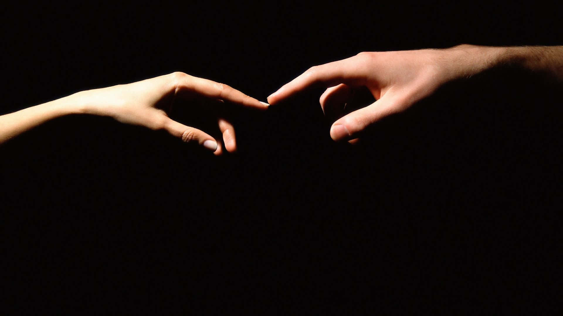 hand 桌布 壁紙 — 在戲劇性的聚光燈下，兩隻手穿過黑暗伸出，指尖幾乎觸碰。
