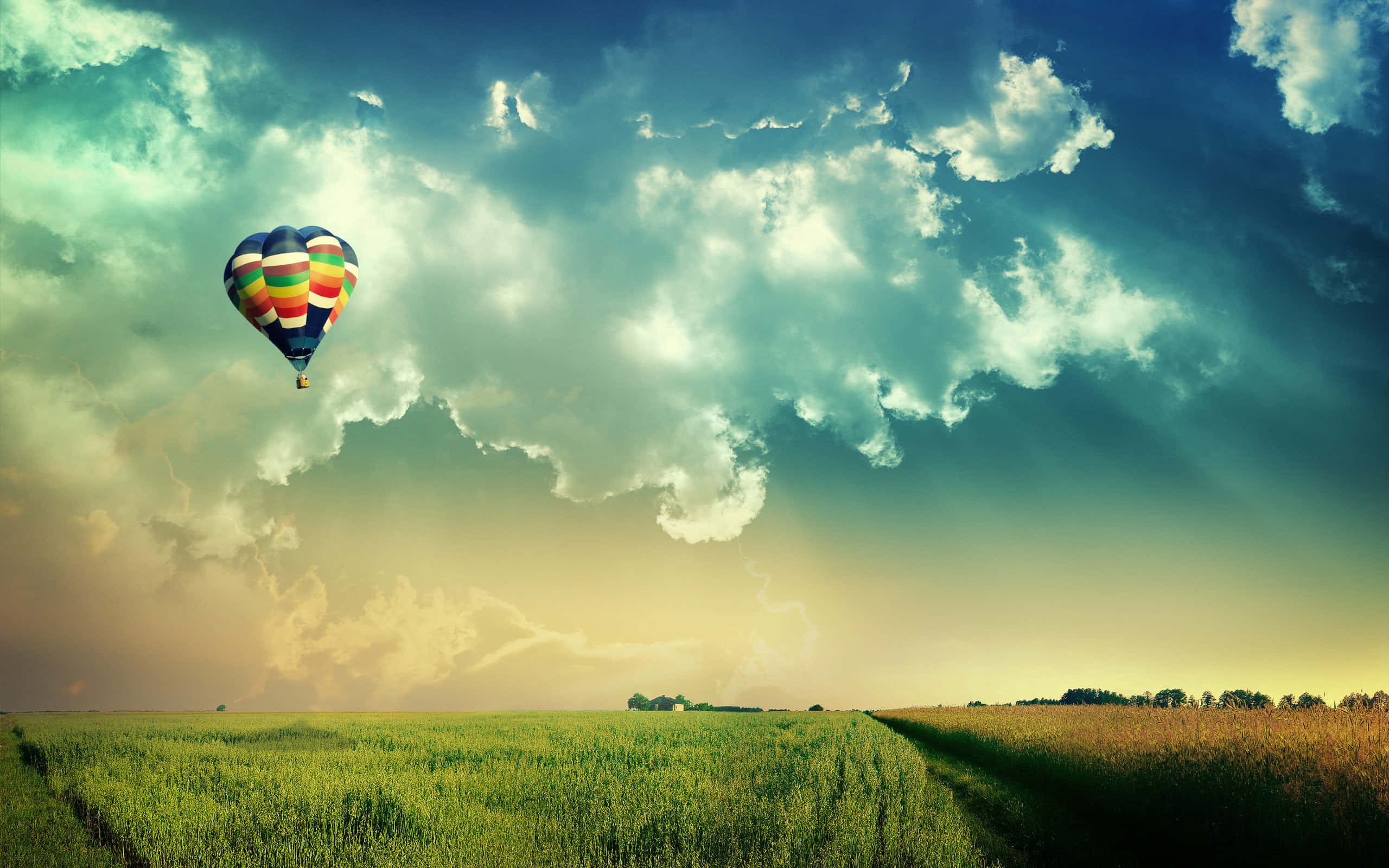 Hot Air Balloon 桌布 壁紙 — 在日落時分戲劇性的多雲天空下，一個色彩繽紛的熱氣球漂浮在廣闊的綠色田野上空。