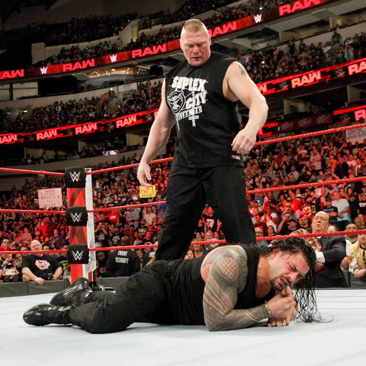 Roman Reigns 桌布 壁紙 — 在明亮的場館燈光下，摔角手布洛克·雷斯納（Brock Lesnar）居高臨下，俯視被壓制在WWE擂台墊上的羅曼·雷恩斯（Roman Reigns）。