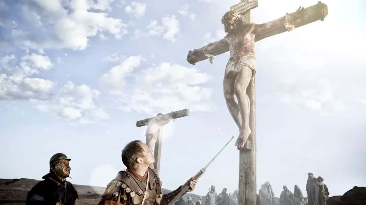 Son Of God 桌布 壁紙 — 在明亮的天空下，耶穌被釘在木製十字架上的戲劇性描繪，下方有羅馬士兵和旁觀者。