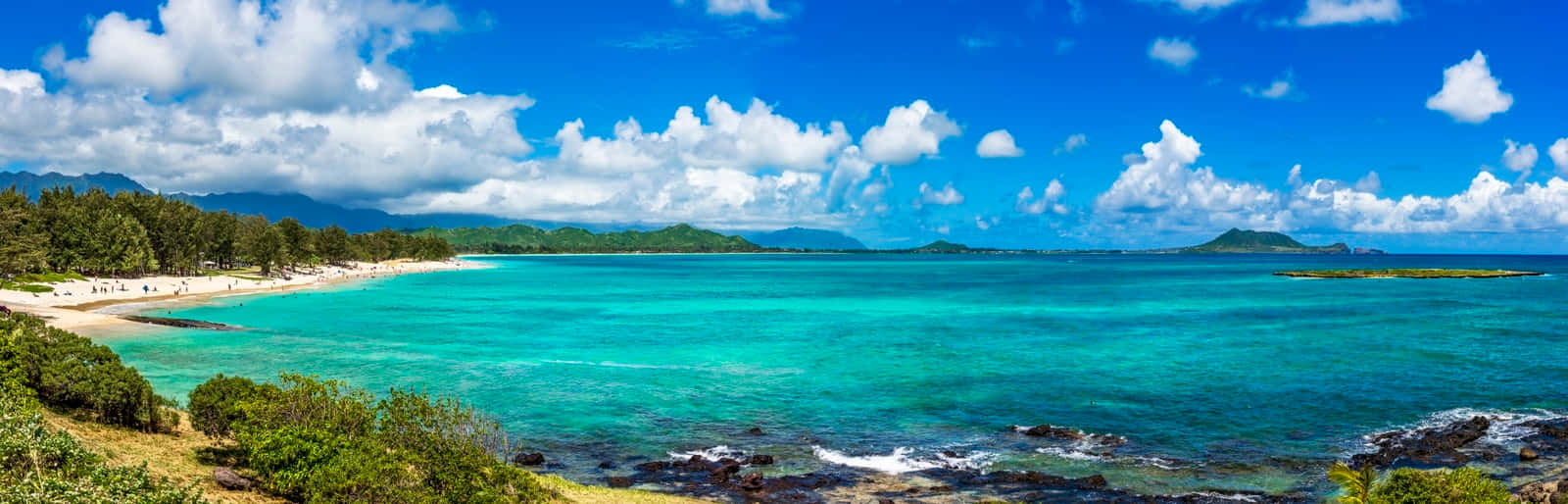 Hawaiian Island 桌布 壁紙 — 在明亮的藍天下，一個碧綠色的熱帶海灣全景，擁有白色沙灘、綠色山丘和蓬鬆的白雲。