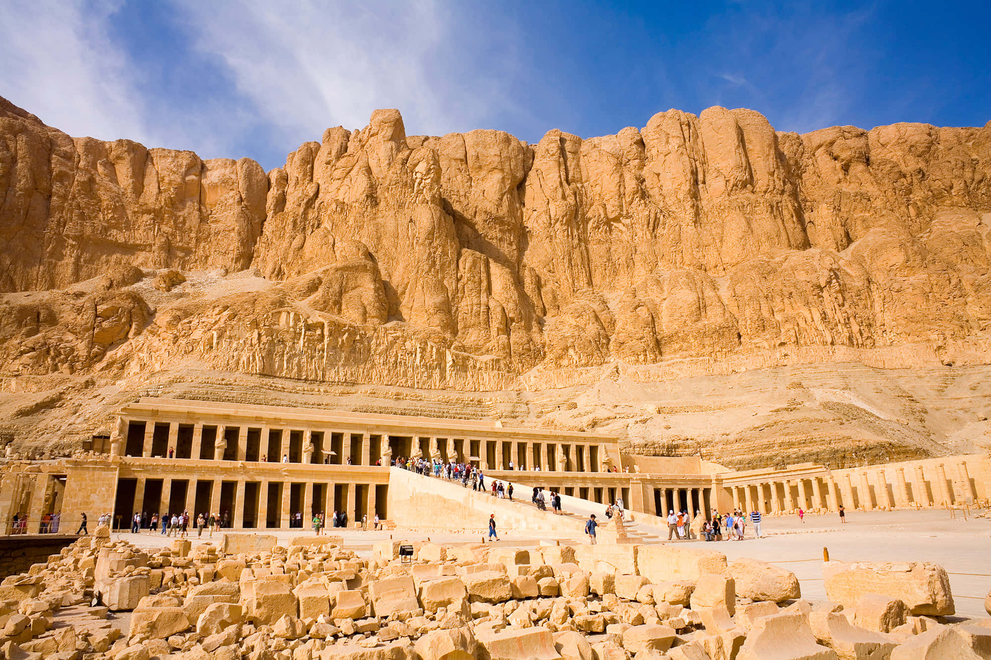 Ancient Egypt 桌布 壁紙 — 在明亮的藍天下，雕刻在金色懸崖上的古埃及神廟，遊客正在探索其宏偉的石階。