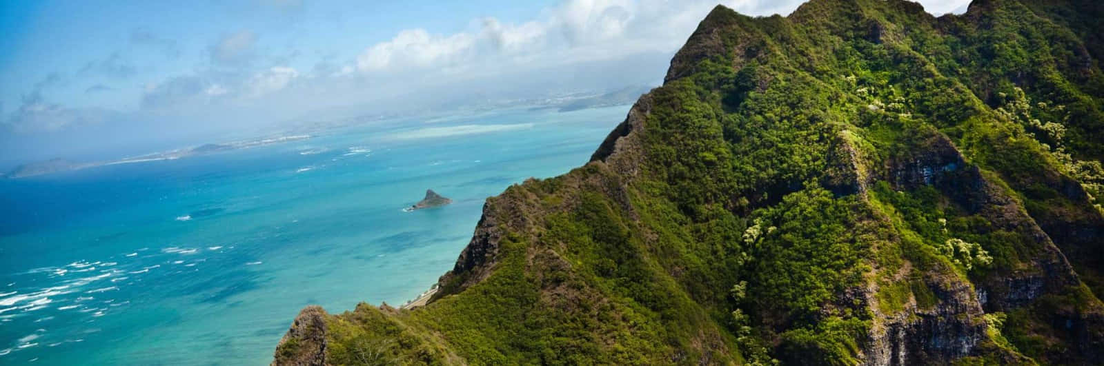 Hawaiian Island 桌布 壁紙 — 在明亮的藍天下，鬱鬱蔥蔥的綠色山脈墜入充滿活力的綠松石色海水中的壯麗全景。