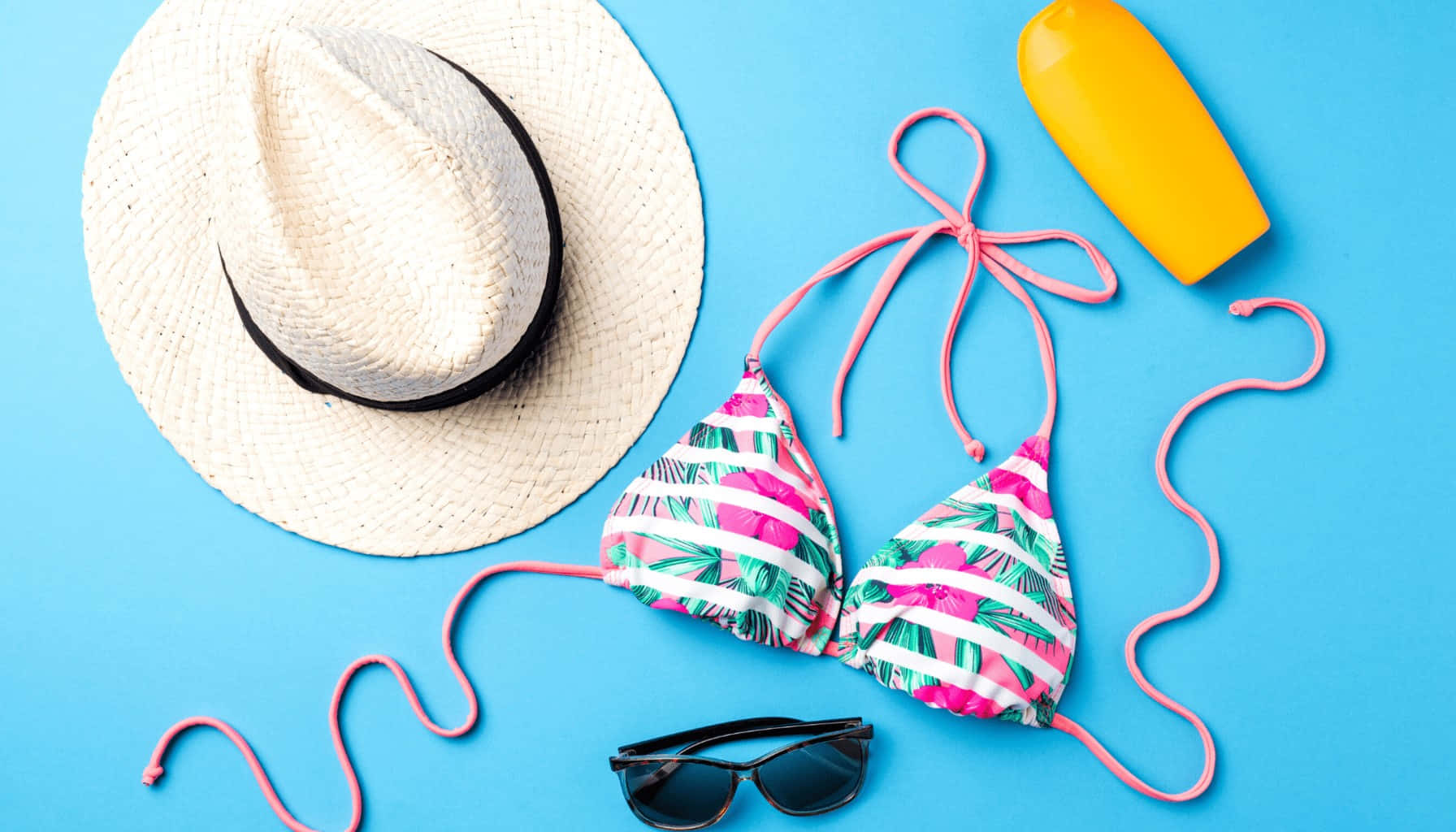 Beach Accessories 桌布 壁紙 — 在明亮的藍色背景上，以鮮豔的平鋪方式展示夏季必需品，包括草帽、比基尼、太陽眼鏡和防曬霜。