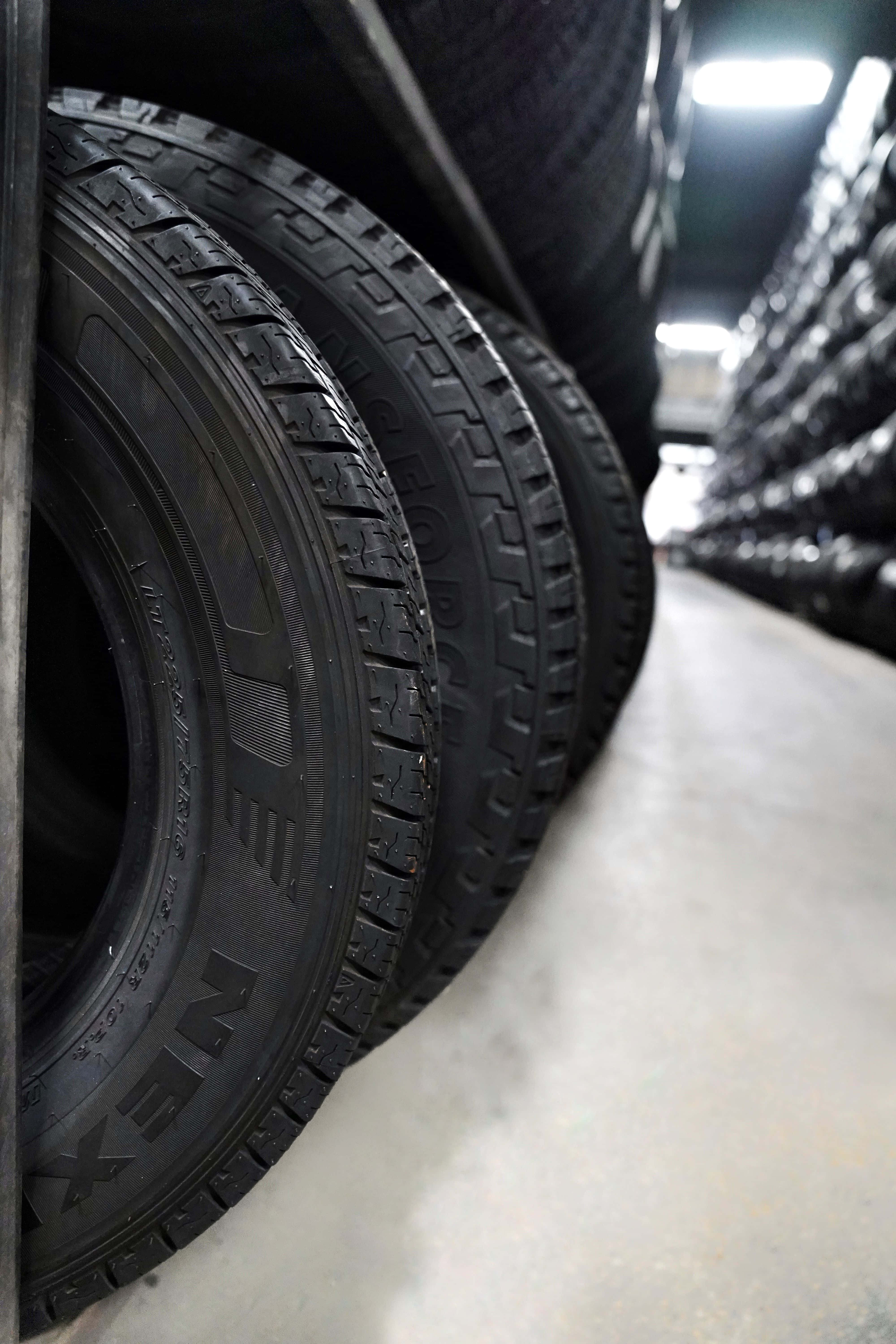 Winter Tires 桌布 壁紙 — 在明亮的螢光燈下，倉庫通道中堆疊的黑色輪胎行。