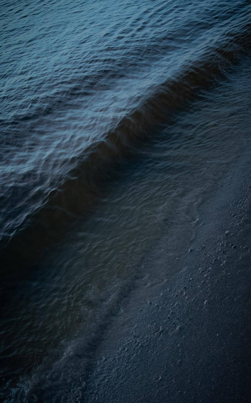海洋 桌布 壁紙 — 在昏暗燈光下，深藍色海浪在黑色沙灘上緩緩退去的特寫。