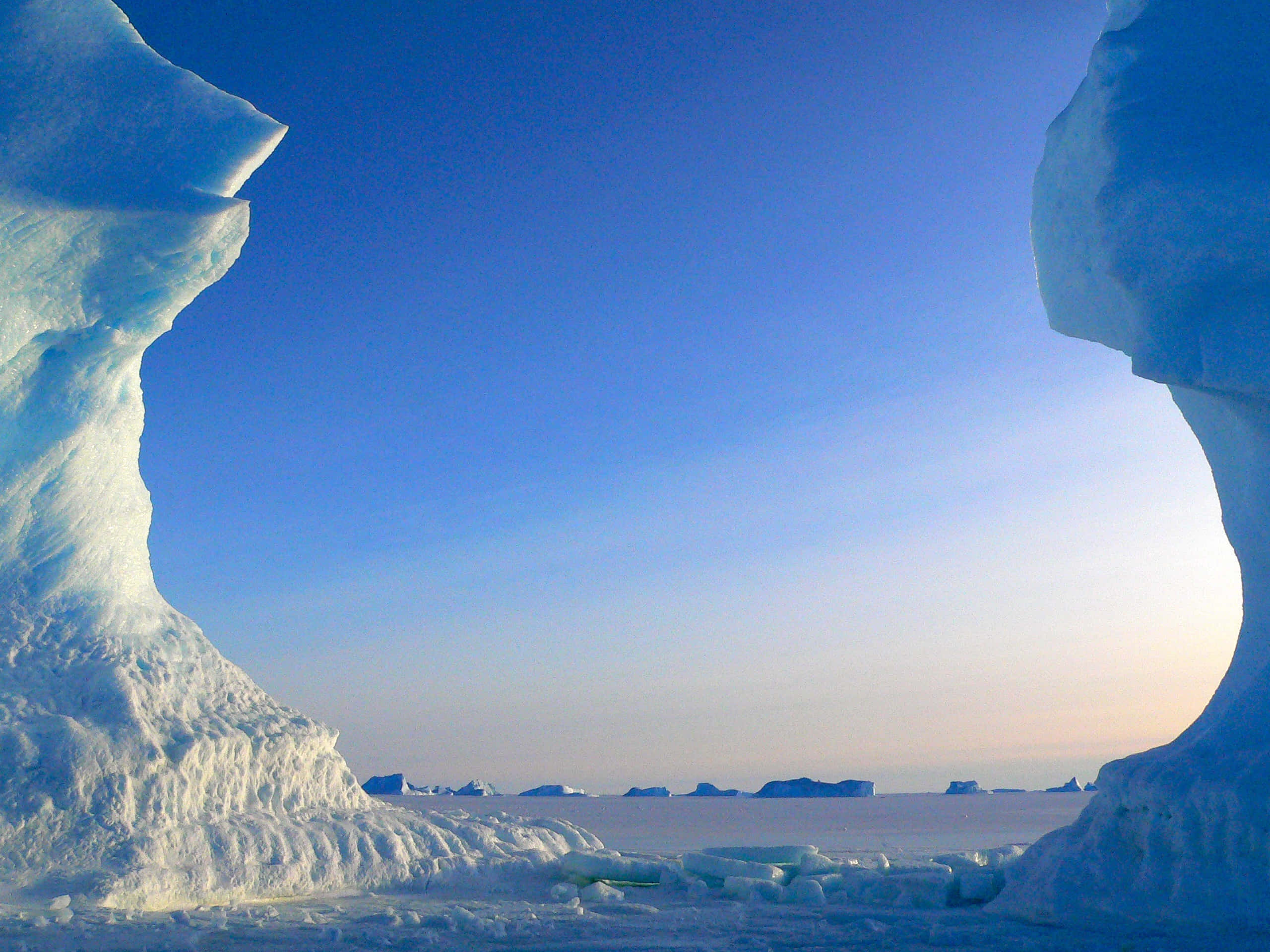 Antarctica 桌布 壁紙 — 在晴朗的藍天下，兩座高聳的冰層形成壯麗的北極景觀，遠方有冰山。