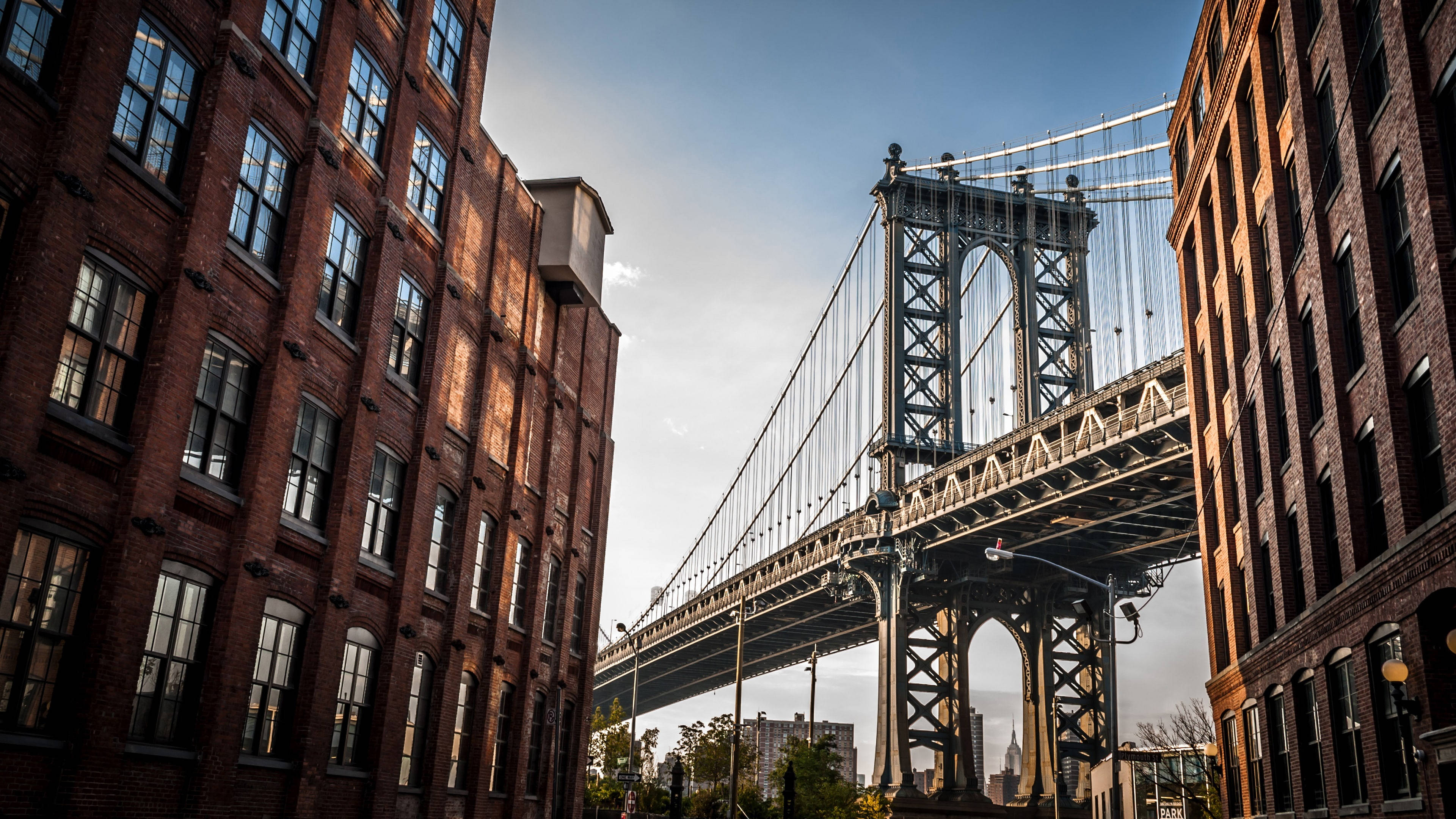 New York 桌布 壁紙 — 在晴朗藍天下，由高聳磚砌建築物框住的曼哈頓大橋低角度景觀。