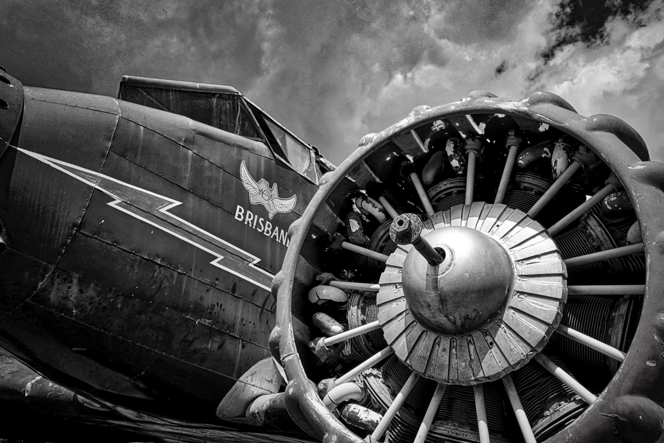 Jet Engine 桌布 壁紙 — 在暴風雨的天空下，以低角度拍攝的戲劇性黑白照片，展示復古螺旋槳飛機的引擎和機身。