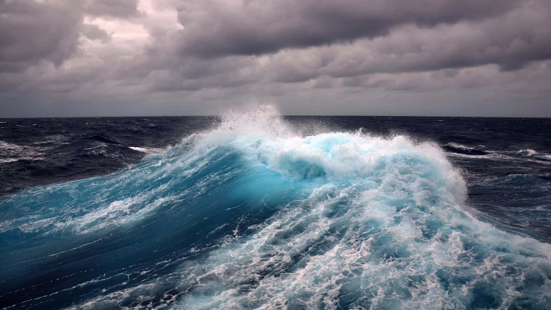 海浪 桌布 壁紙 — 在暴風雨的海洋中，巨大的藍綠色波浪在沉重的灰色天空下破碎。
