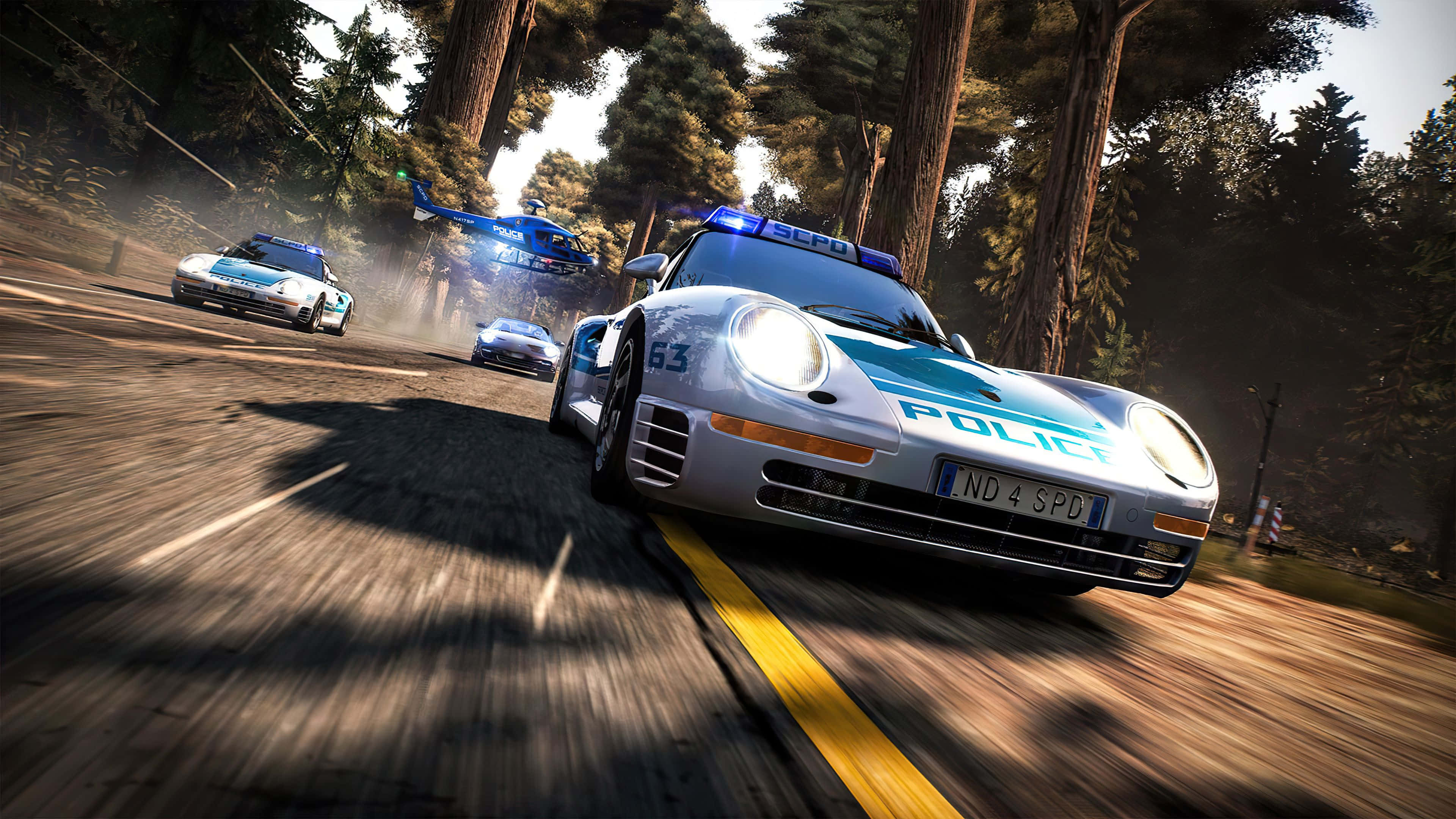 在最佳《Need for Speed》中超越對手 壁紙 — 高速警匪追逐在森林道路上展開，一架藍色直升機在上空盤旋，賽車後方塵土飛揚。
