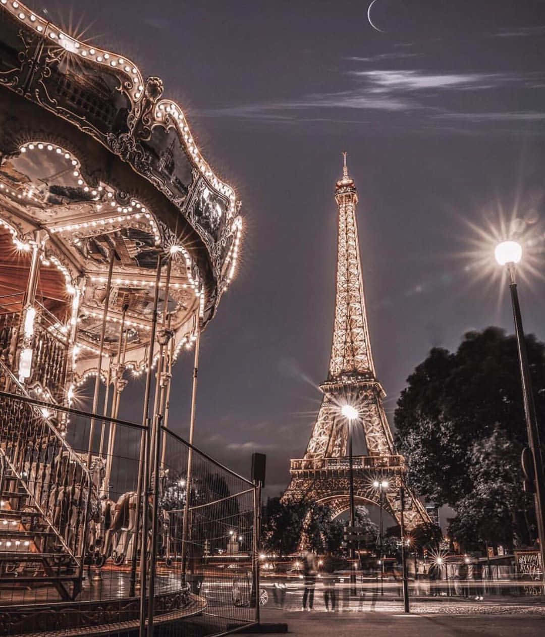 Eiffel Tower 桌布 壁紙 — 在月光下的巴黎夜空，一個發光的旋轉木馬矗立在燈火通明的艾菲爾鐵塔旁。