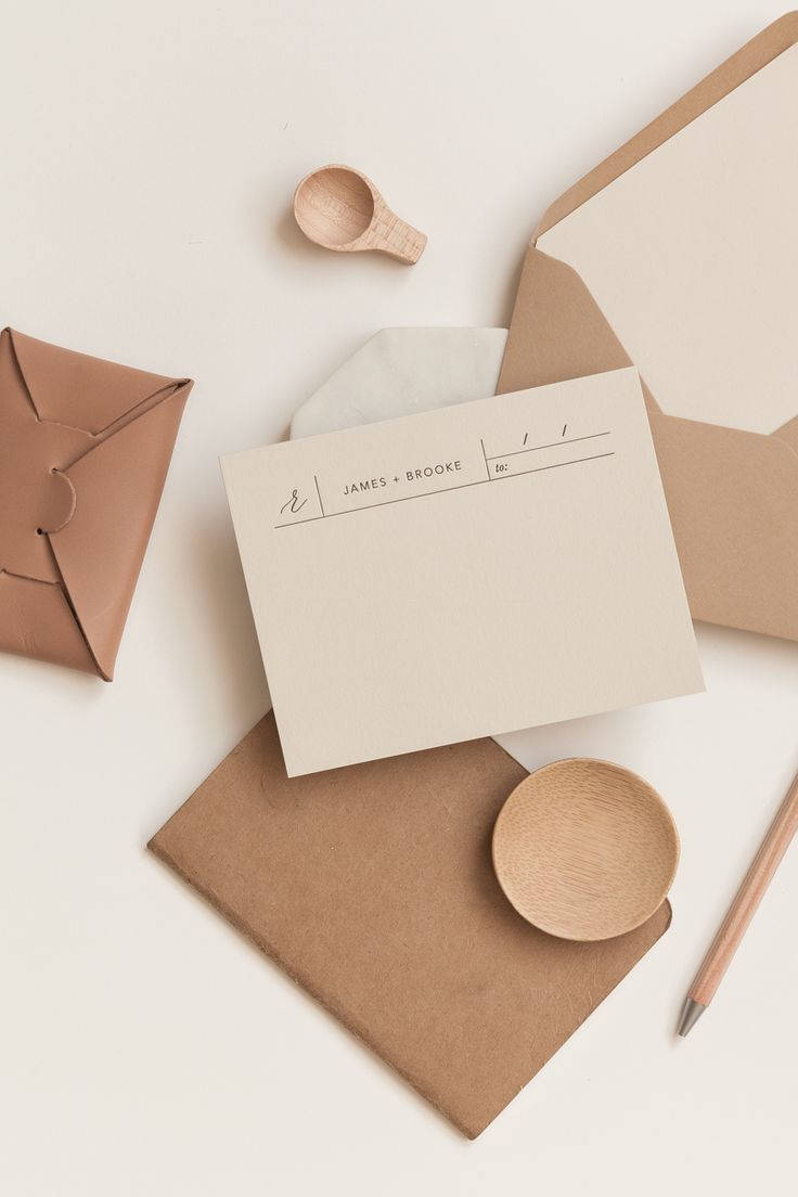 Beige Minimalist 桌布 壁紙 — 在柔軟的白色表面上，以極簡風格平鋪擺放米色文具信封和木質配件。