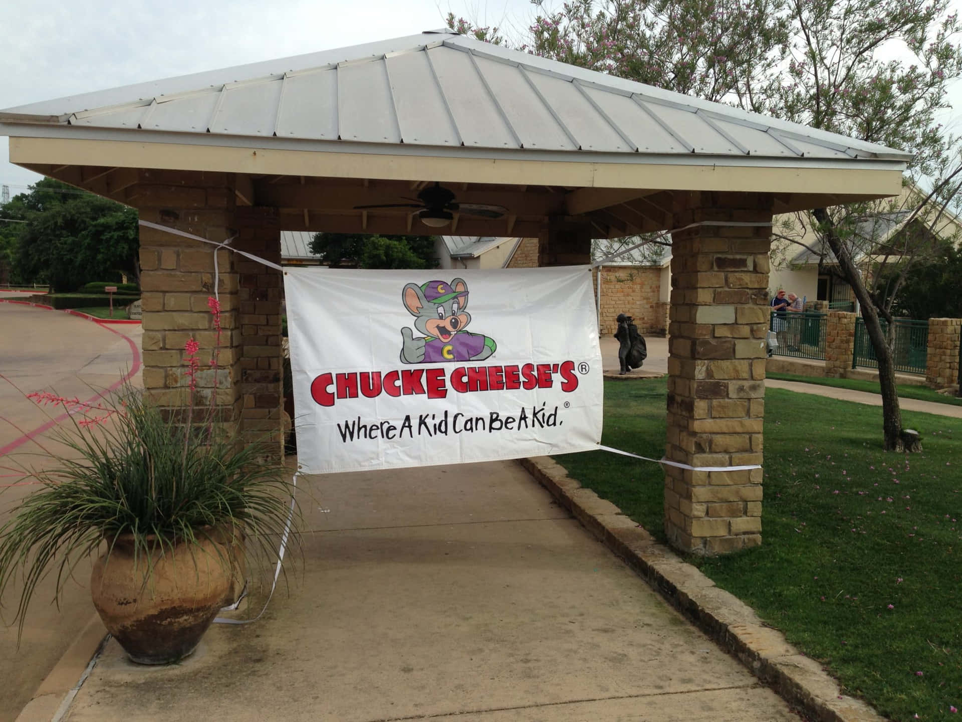 室外入口處的 Chuck E Cheese 橫幅，配有石柱和草地。
