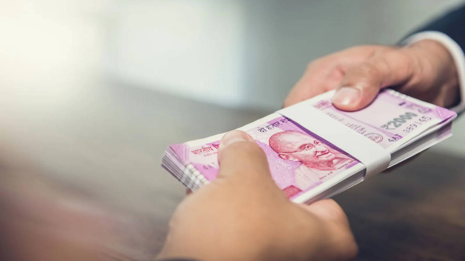 Indian 桌布 壁紙 — 在模糊的室內環境中，兩隻手交換一疊用白色帶子捆綁的印度2000盧比鈔票。