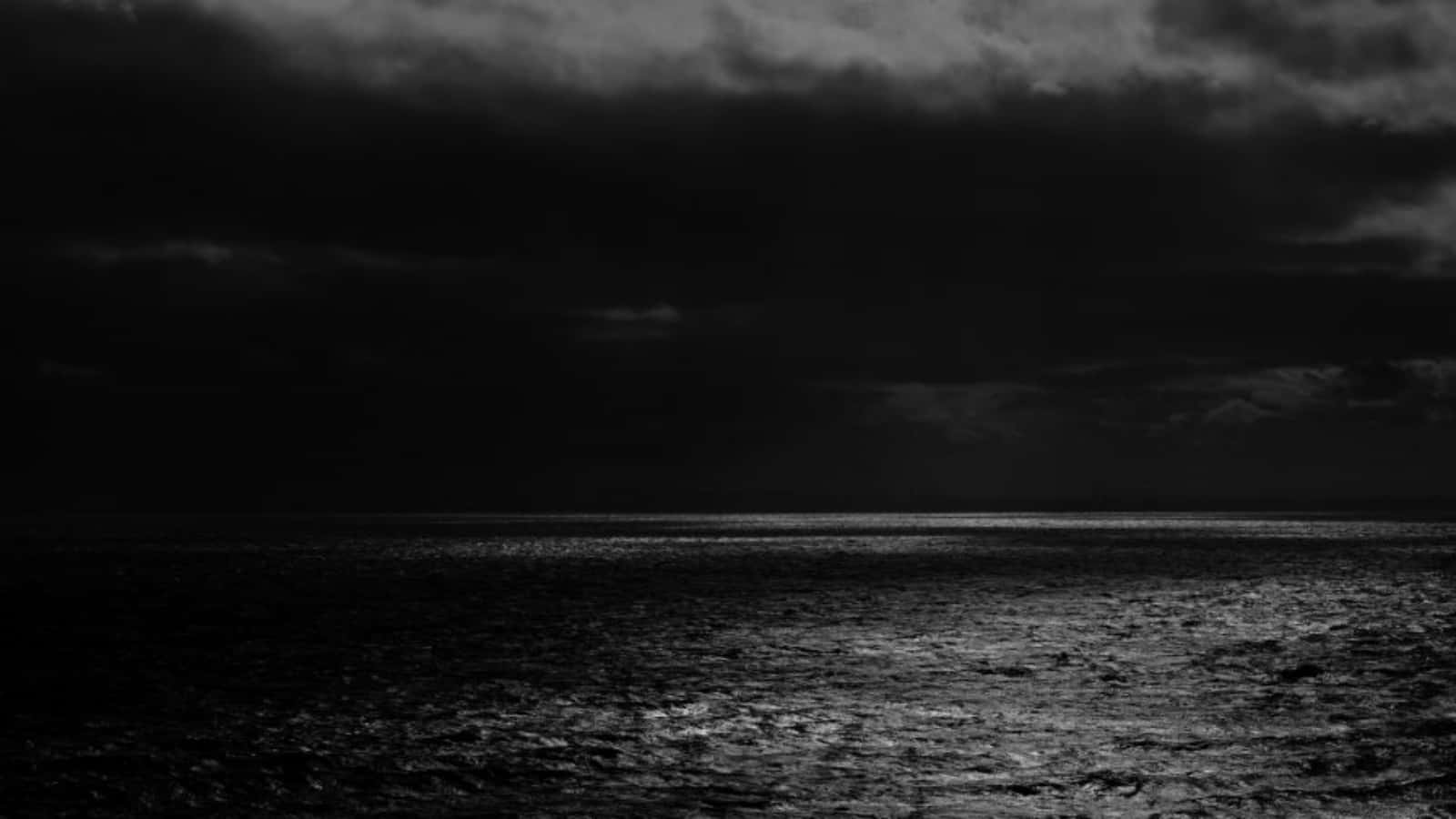 Black Sea 桌布 壁紙 — 在沉重風暴天空下，微弱光線穿過雲層的單色海景。