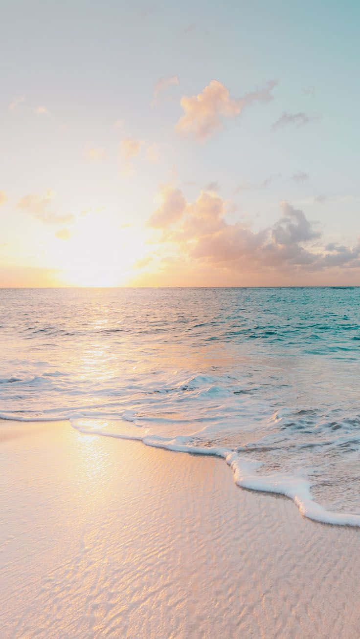 在海灘上悠閒享受夏日陽光 壁紙 — 金色夕陽海浪輕輕親吻柔軟粉紅沙灘，在粉彩天空雲朵下。
