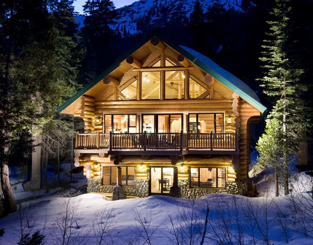 Cozy Winter Cabin 桌布 壁紙 — 在深藍色夜空下，一間舒適的木屋在白雪覆蓋的山脈背景下溫暖地發光。