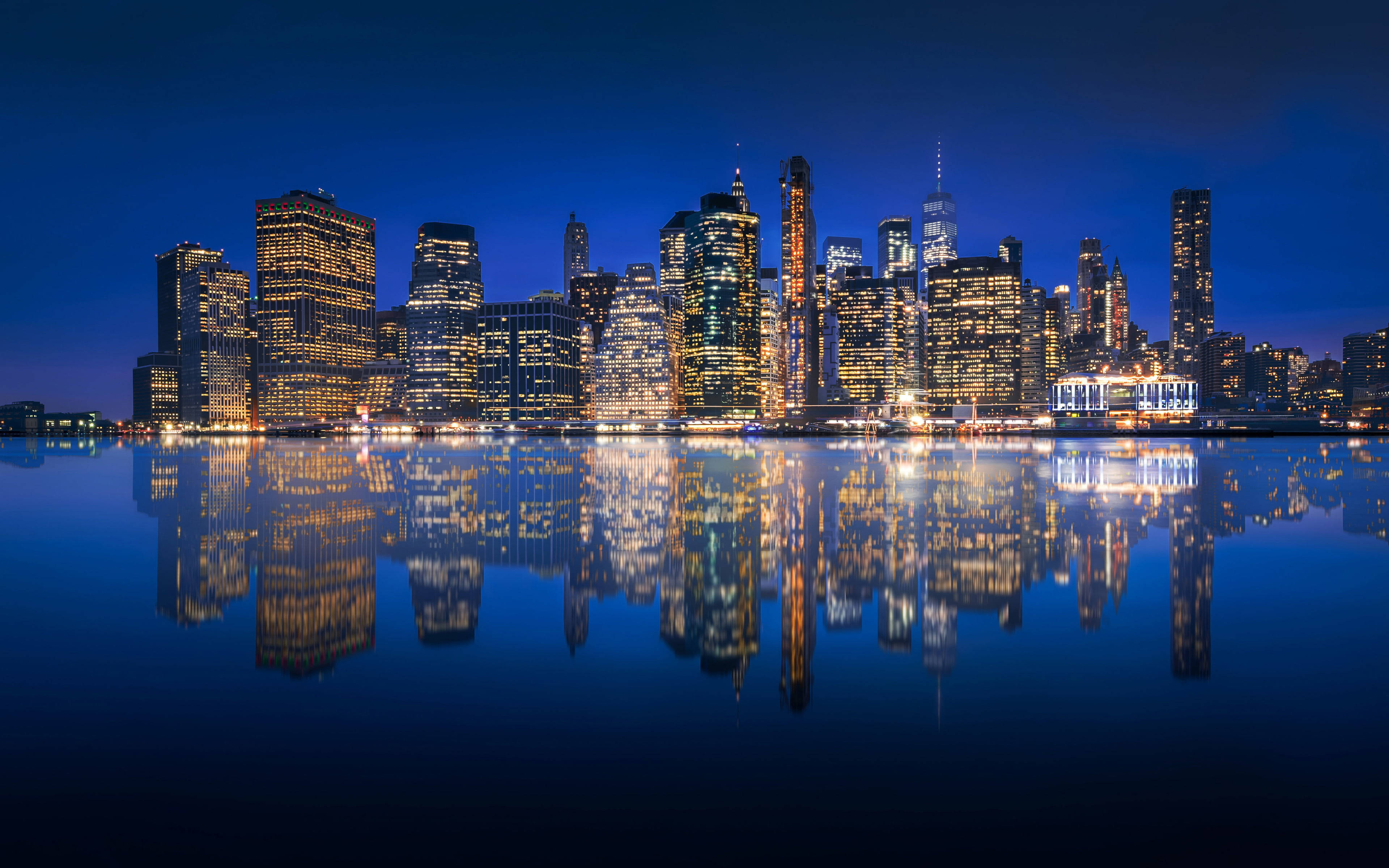 new york 4K 桌布 壁紙 — 在深藍色天空下，摩天大樓閃爍著溫暖燈光，完美倒映在平靜水面上，令人驚嘆的夜景。