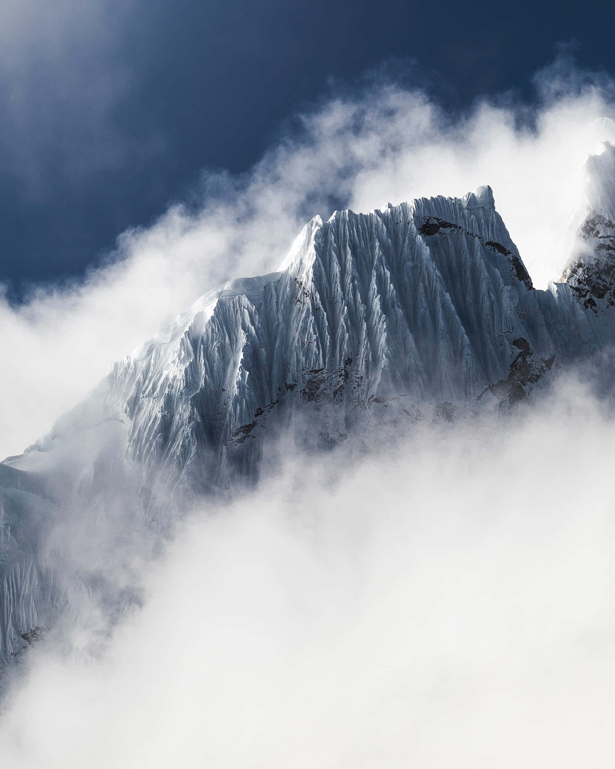 寒冷 桌布 壁紙 — 在深藍色的天空下，鋸齒狀的積雪山峰刺穿旋轉的雲層。