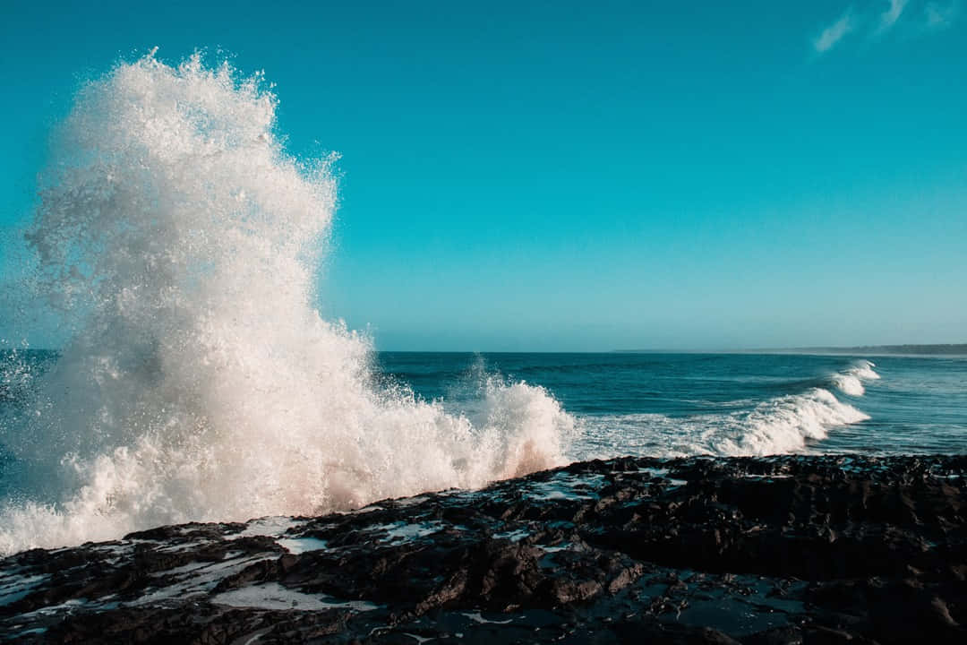 Beach Waves 桌布 壁紙 — 在清澈的碧藍天空下，強勁的海浪衝擊著深色火山岩。