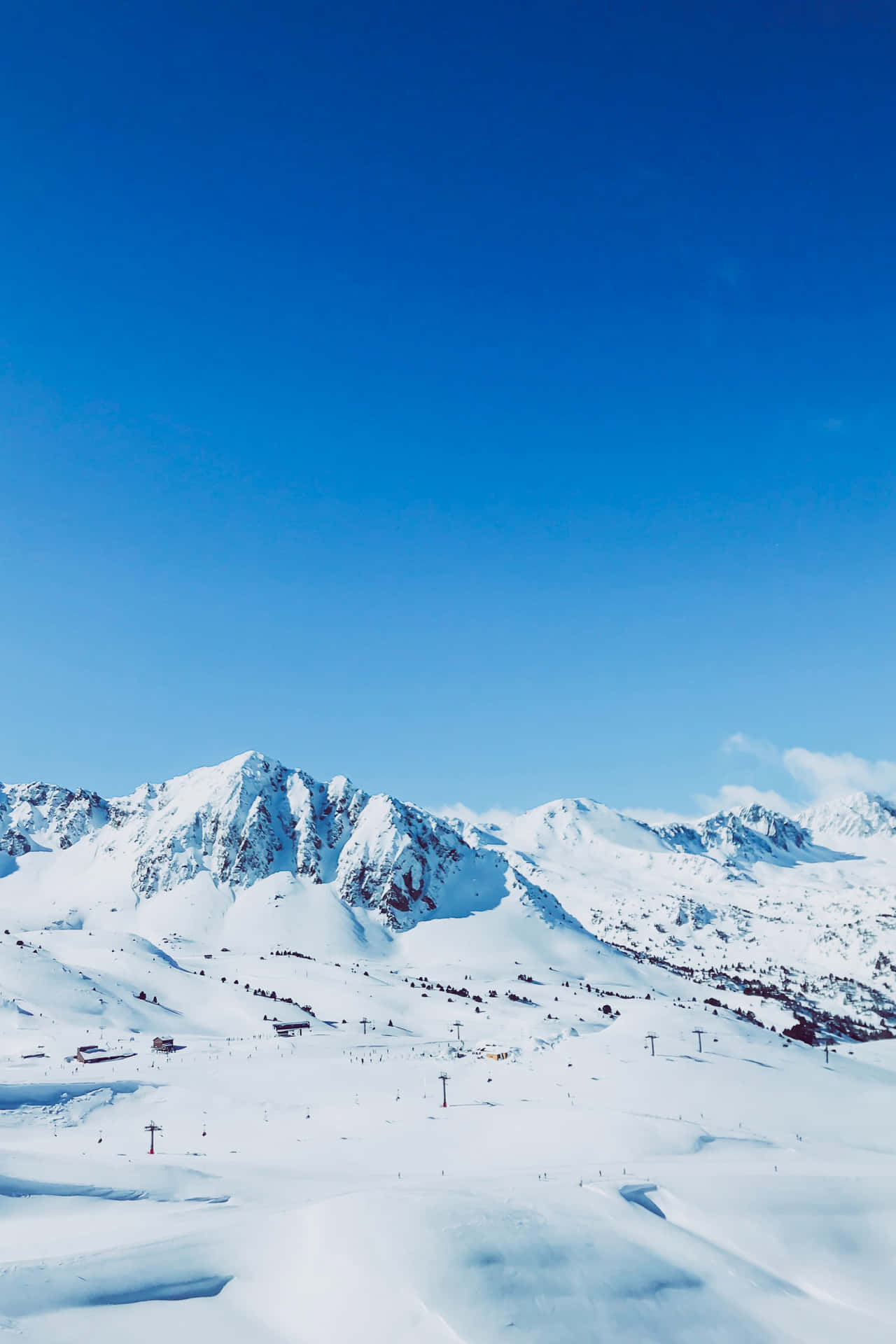 白雪覆蓋的山脈，有滑雪纜車和小型建築，在清澈的藍天下。