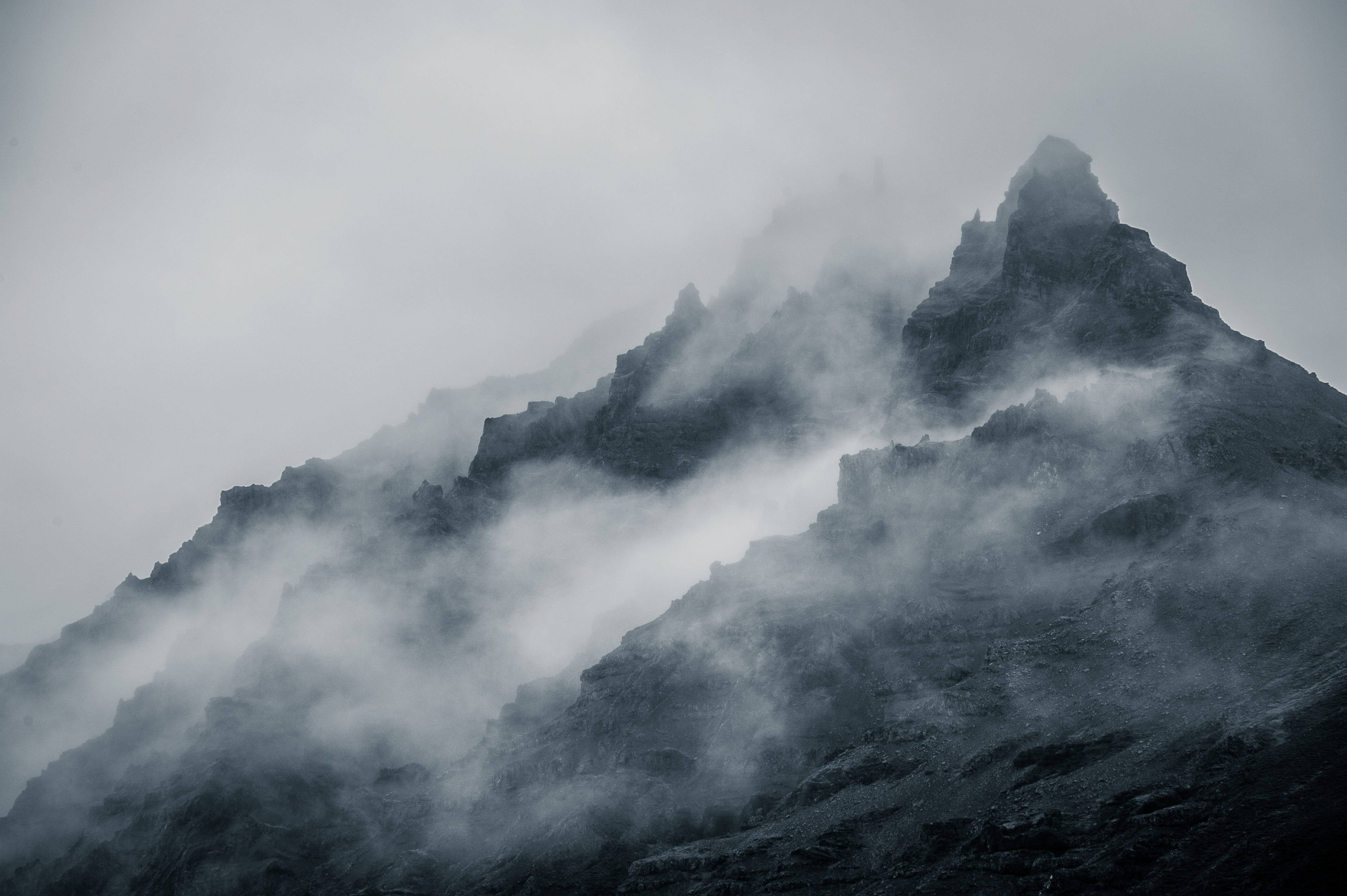 Mountain 桌布 壁紙 — 在灰色天空下，鋸齒狀的山峰穿過旋轉的迷霧，呈現出陰鬱的黑白景觀。