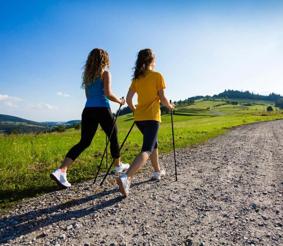 兩位女士在碎石路上手持行山杖，穿過起伏的綠色山丘徒步。