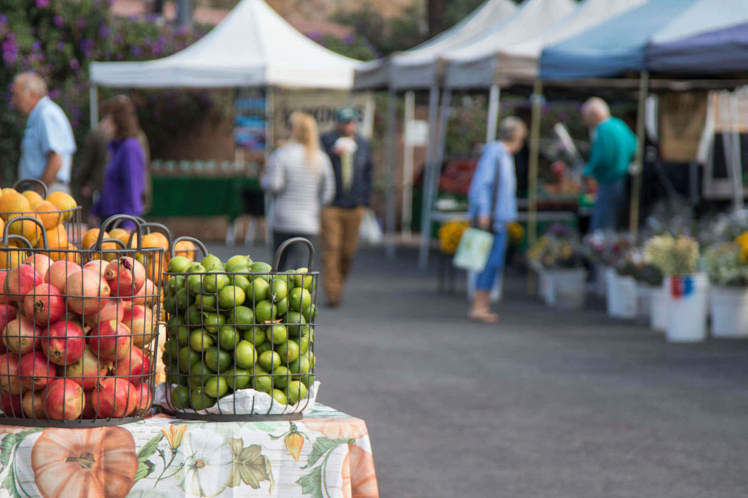 Farmers Market 桌布 壁紙 — 在熙熙攘攘的戶外農貿市場，花桌布上擺放著一籃籃鮮豔的紅蘋果和青檸。
