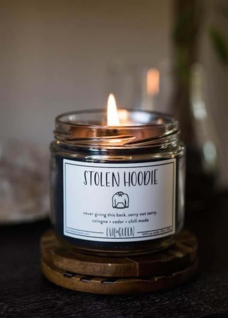 在昏暗房間的木製杯墊上，點燃的蠟燭帶有「STOLEN HOODIE」標籤。