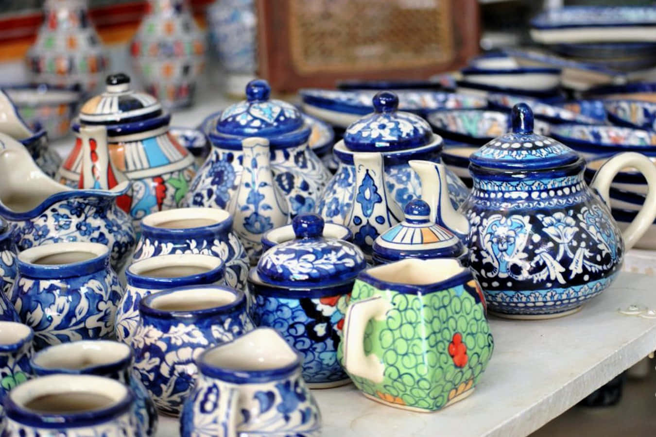 Ceramic 桌布 壁紙 — 在白色表面上展示色彩鮮豔的手繪陶瓷茶壺和罐子，帶有藍色花卉圖案和彩色點綴。