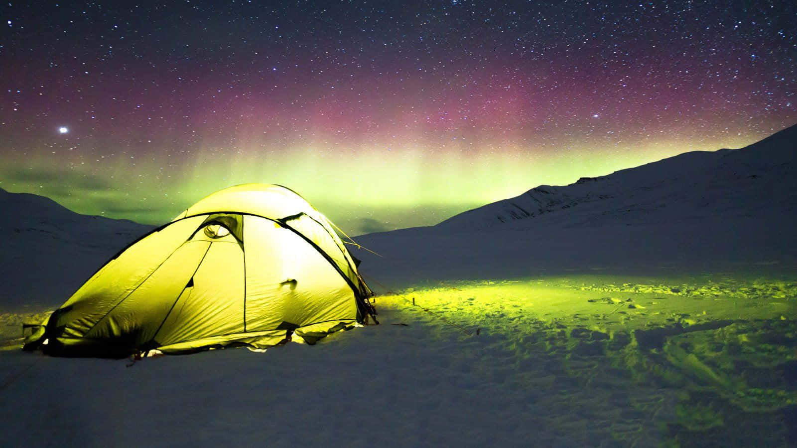 Winter Camping 桌布 壁紙 — 在白雪覆蓋的山巒中，一頂發光的黃色帳篷，上方是橫跨星空的鮮綠色和紫色極光。