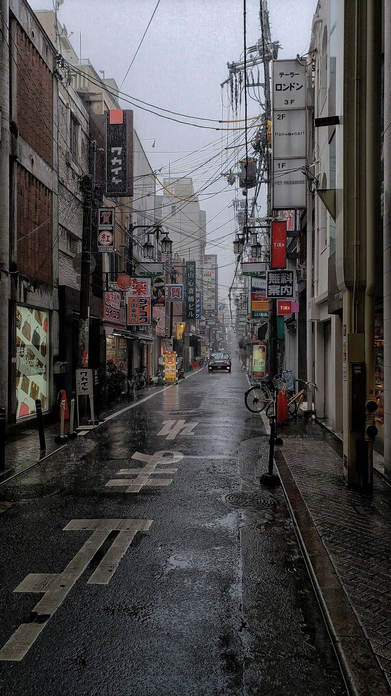 在簡約中發現美：灰色美學 壁紙 — 雨中的日本街道，濕漉漉的路面反射著霓虹燈招牌和高樓之間的架空電線。