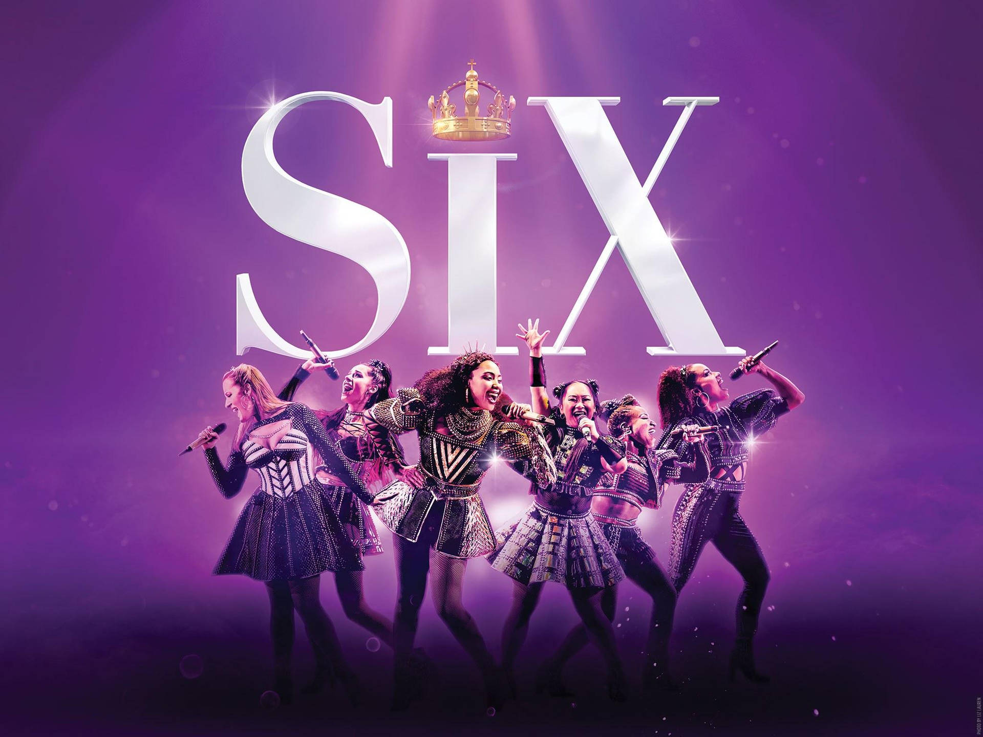 六位身穿閃亮服裝的女王在紫色燈光的舞台上唱歌，背景有大型「SIX」標誌和皇冠。