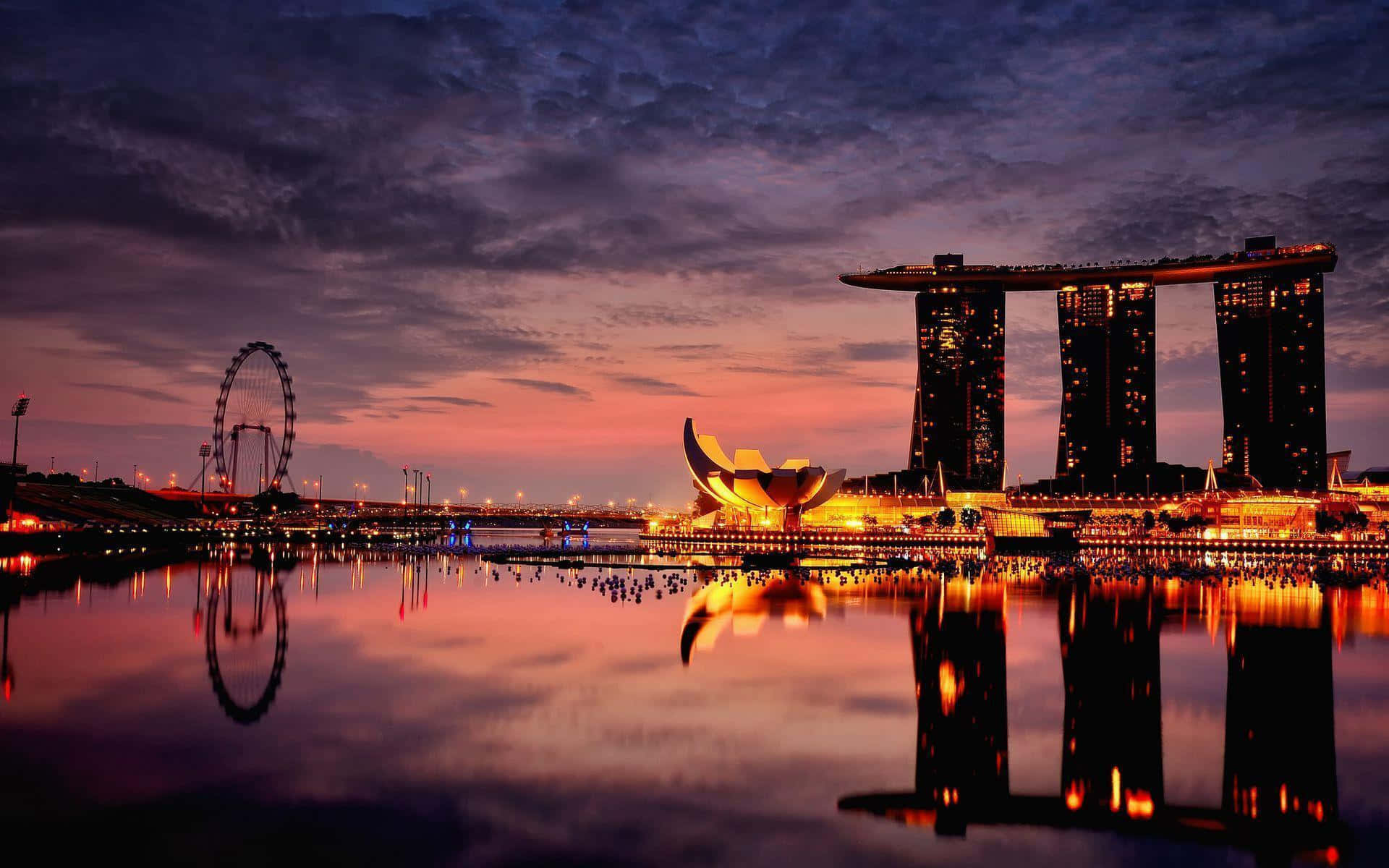 Singapore 桌布 壁紙 — 在紫橙色天空下，平靜水面上映照著燈火輝煌的摩天大樓和摩天輪，充滿活力的暮色城市景觀。