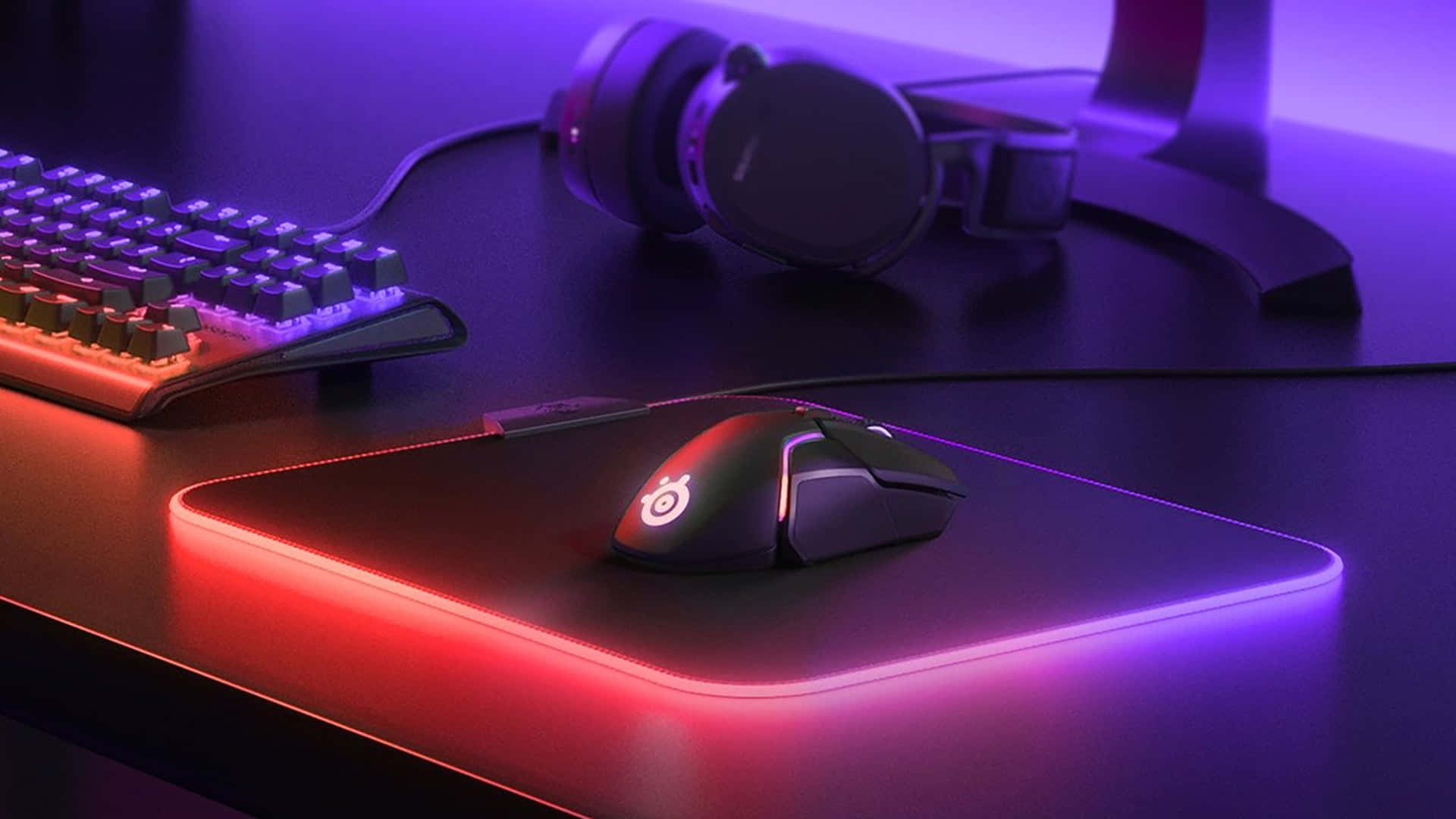 Gaming Mouse 桌布 壁紙 — 在紫紅色環境燈光下，配備發光鍵盤、滑鼠和耳機的遊戲設置。